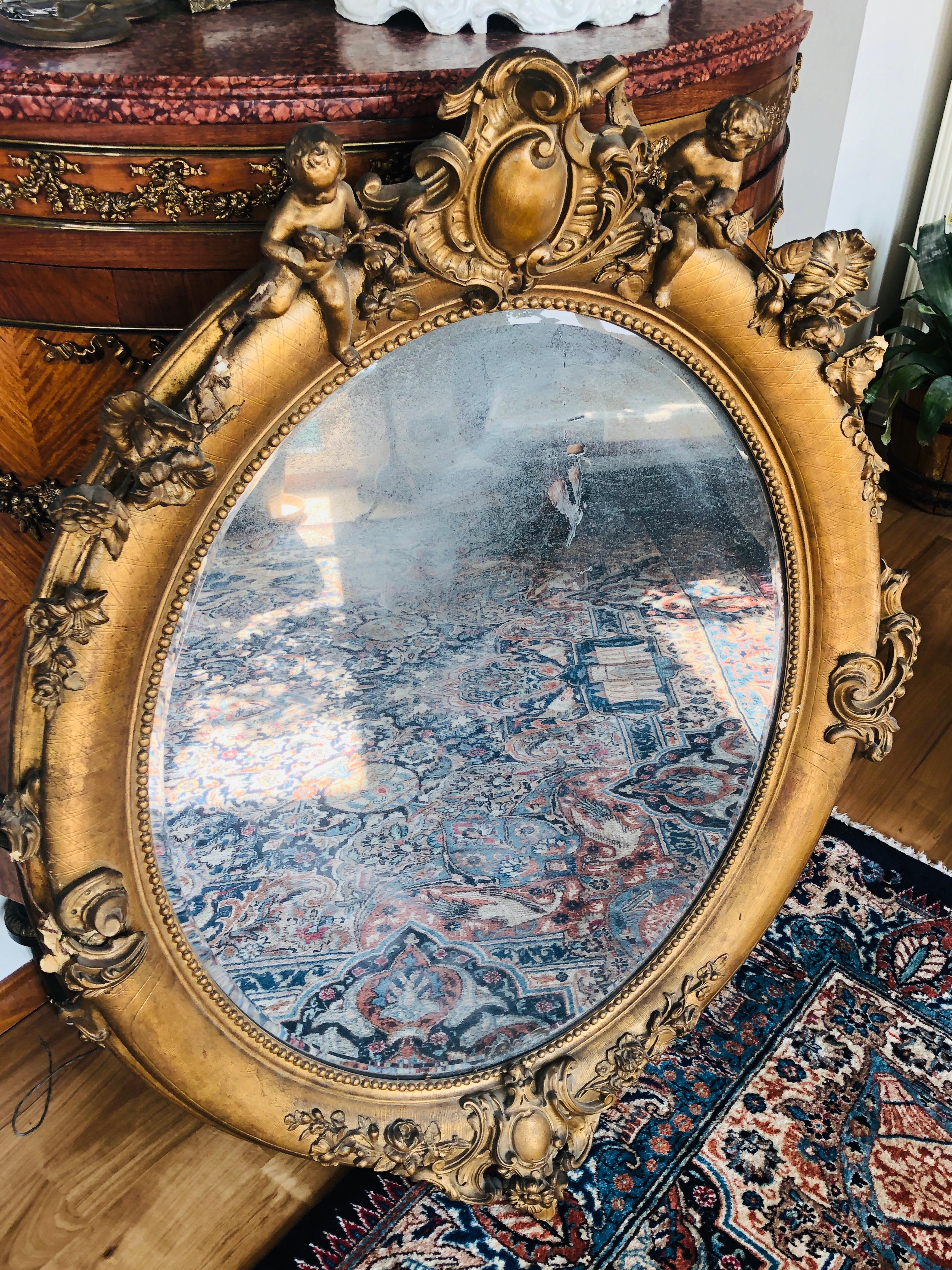 miroir ovale du XIXe siècle d'époque Napoléon III. Bois sculpté, recouvert de gesso et de feuilles d'or. Cette pièce a de beaux ornements et un couple de chérubins sur le dessus et elle porte son verre original.
France, 1860.
  