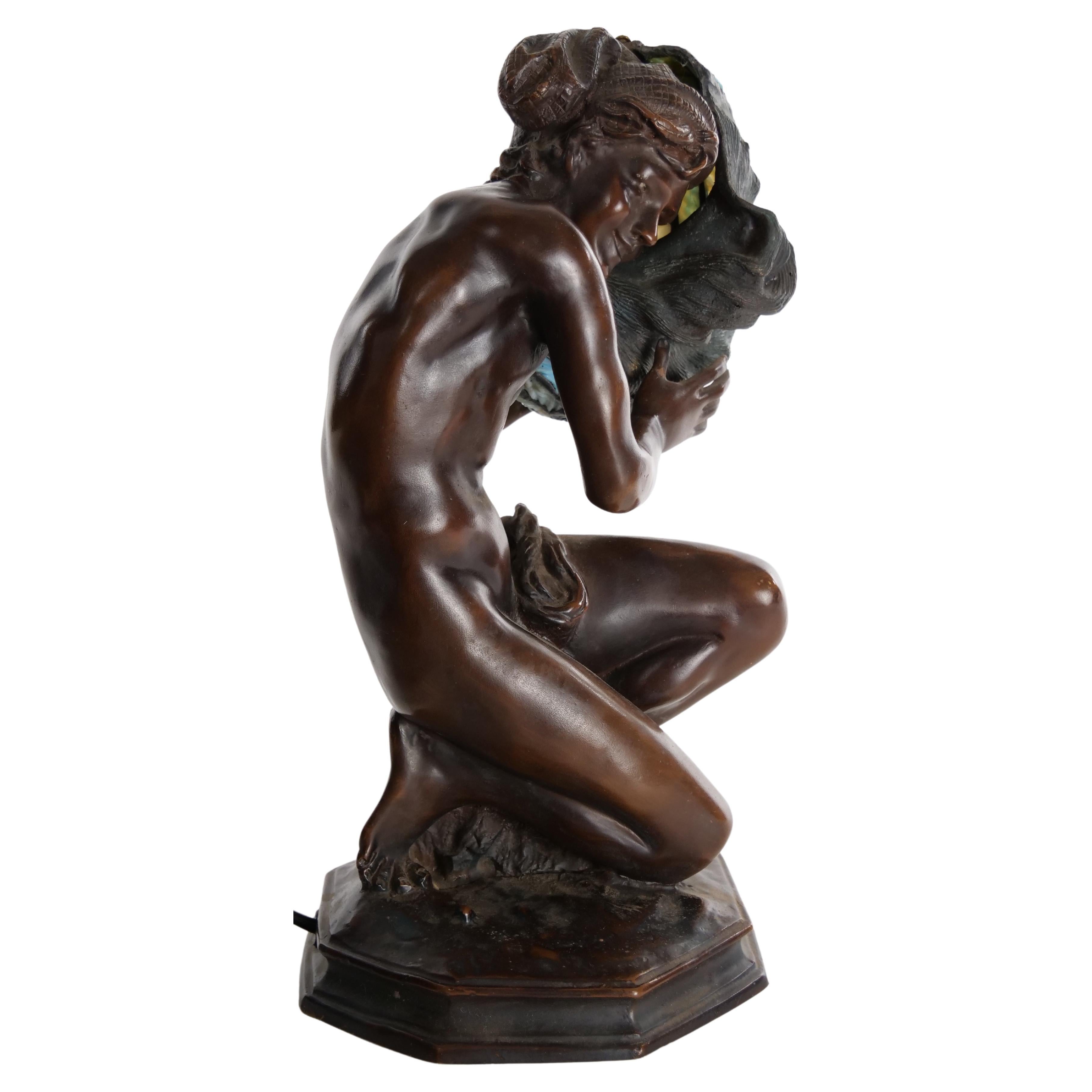 Lampe de table figurée en bronze de la fin du 19e siècle, représentant une femme agenouillée tenant un abat-jour en verre plombé en forme de coquille. La lampe est en bon état de fonctionnement. Usure mineure correspondant à l'âge / à l'utilisation.