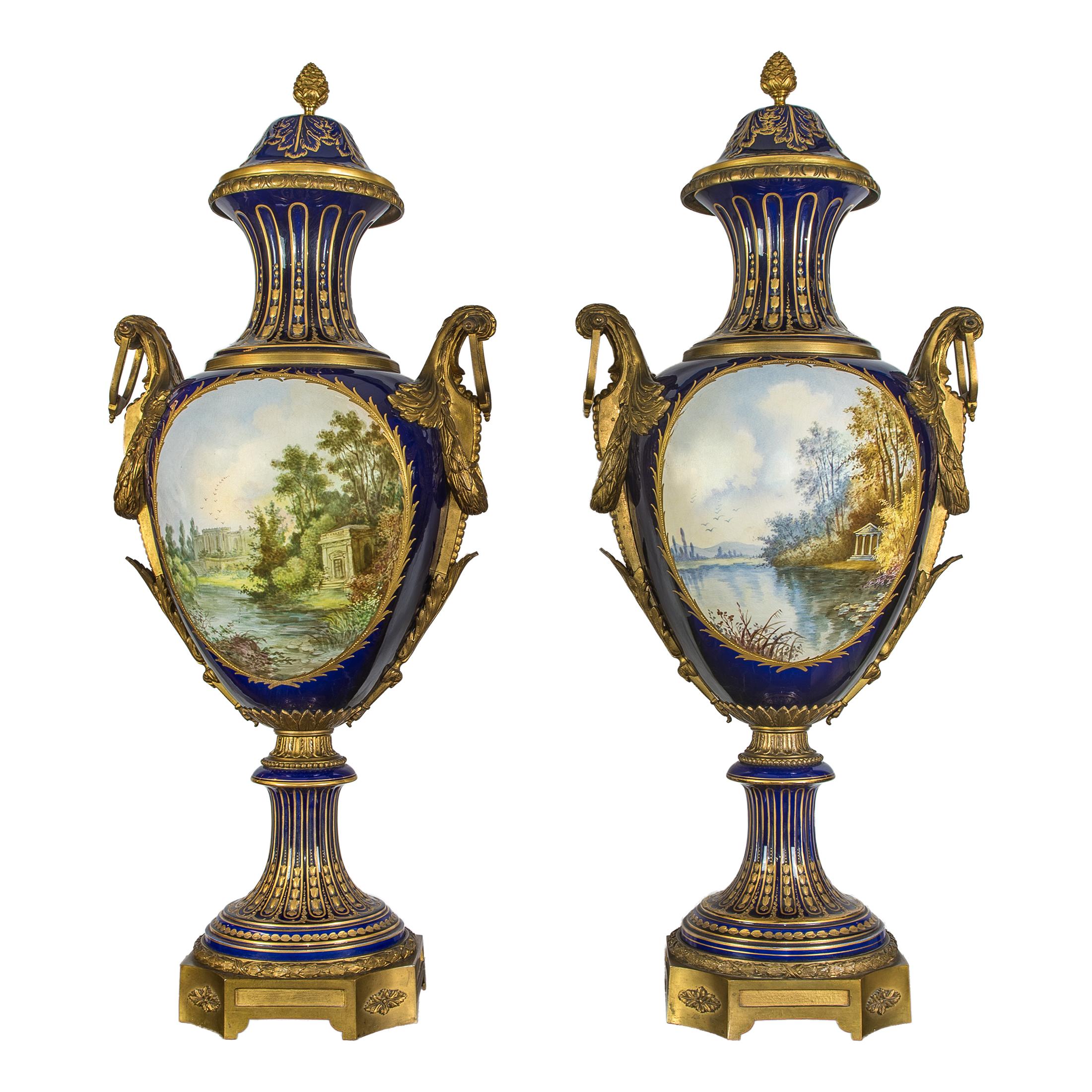 Each cobalt ground with gilding, trumpet-form neck over baluster form body decorated with a figural scene in the garden, reverse with a garden folly, gilt bronze handles, over a collared waist and round socle on shaped base. Provenance: Property of