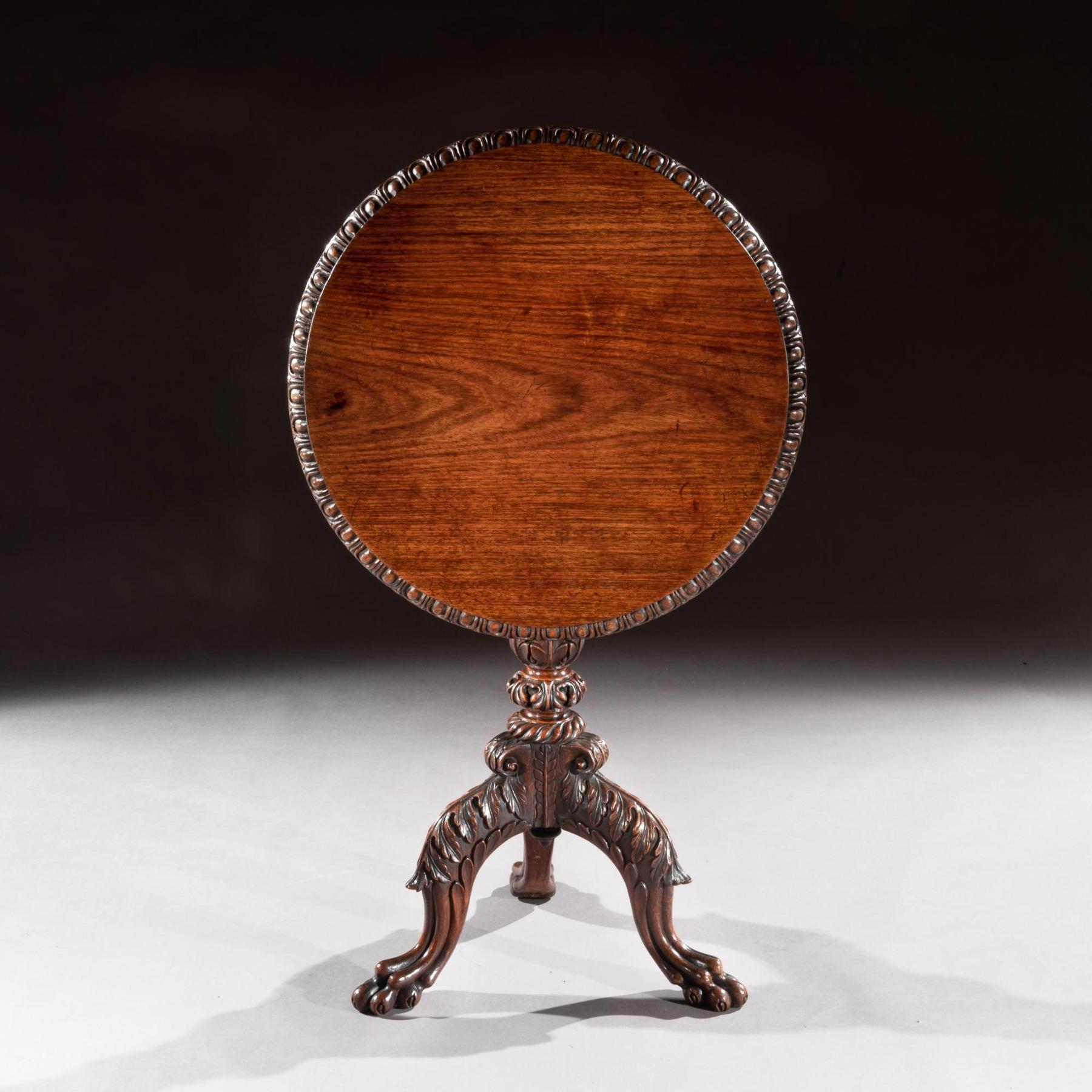 A finely carved with an unusual base 19th century Anglo-Indian solid teak tilt-top tripod / occasional table.

India, Possibly Bombay, circa 1840.

The circular solid teak top with an egg and dart carved edge over an intricately pierced frieze
