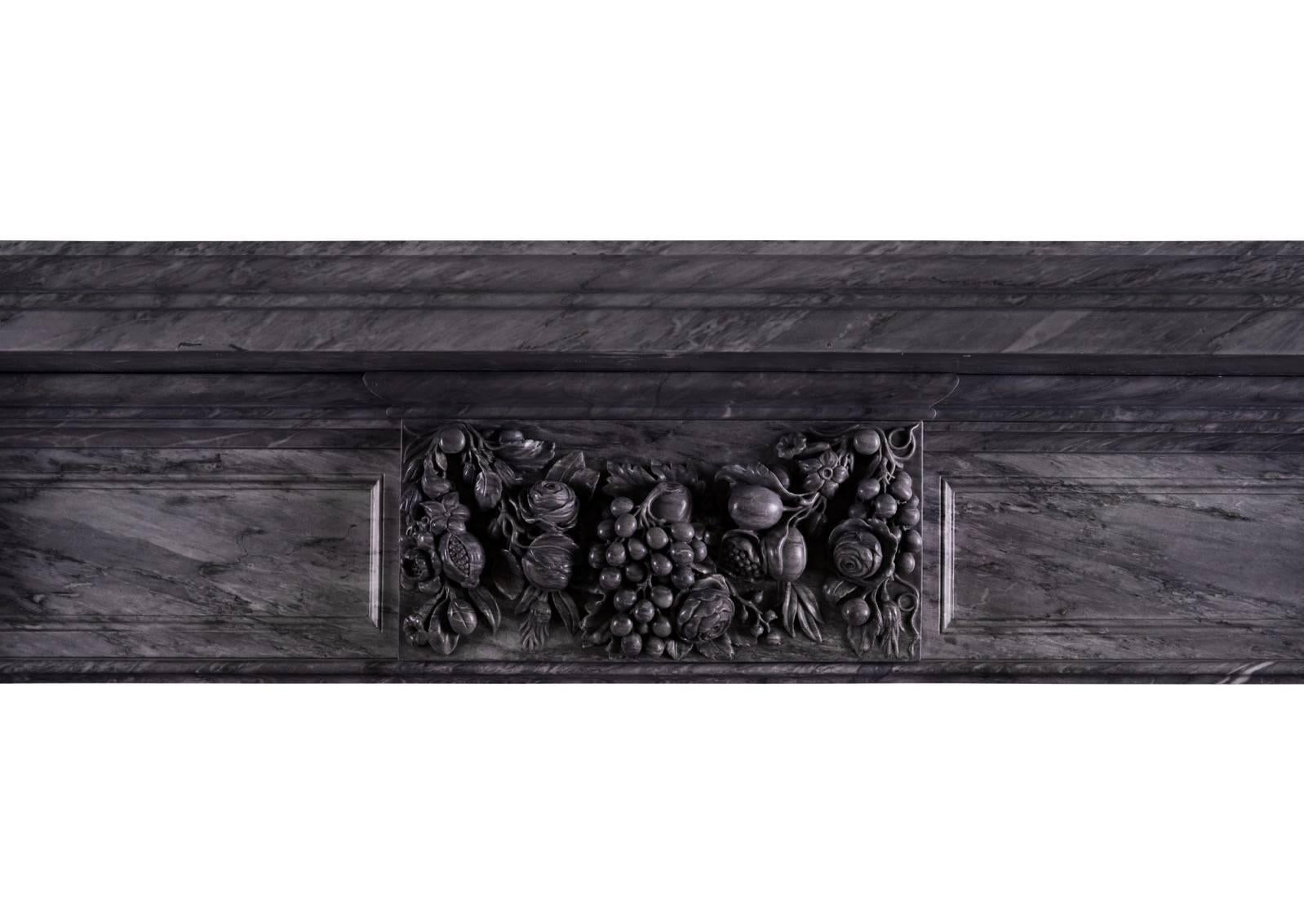 An large and impressive carved fireplace in grey Bardiglio marble. The panelled jambs surmounted by end blocks featuring carved grapes and leaves, the matching centre block with additional flowers and foliage. Moulded shelf above. A very impressive