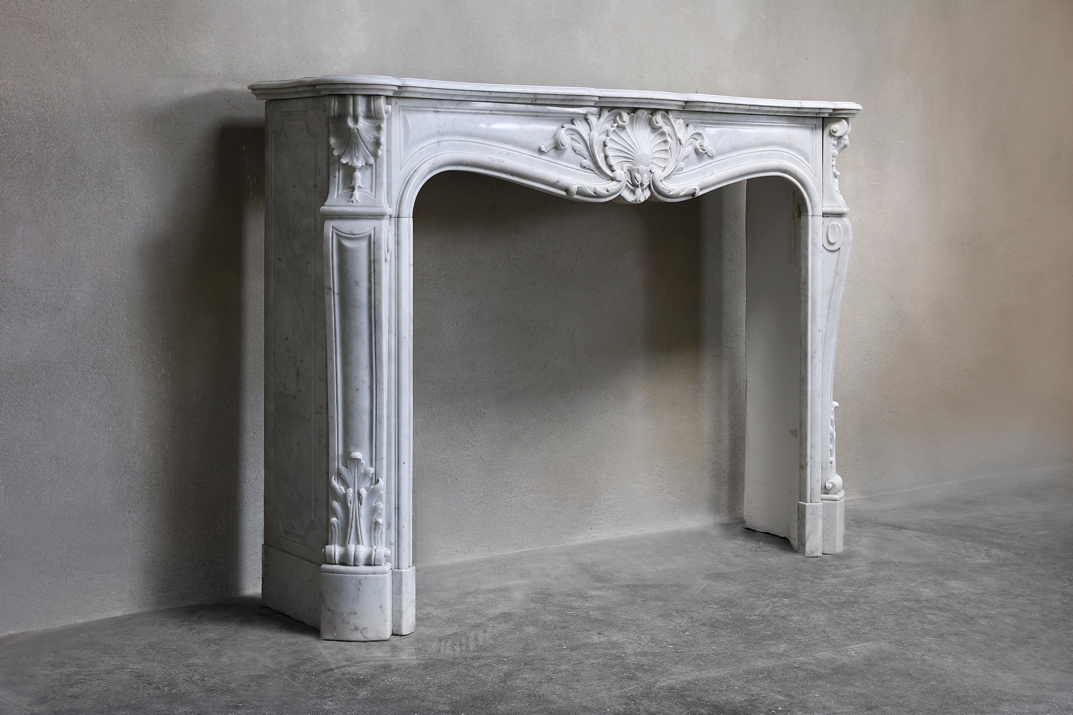 Beautiful antique marble fireplace of Carrara marble in the style of Louis XV from the 19th century. A fireplace with ornate ornaments such as a scallop in the center and on both sides. This chic fireplace fits in a classic as well as a modern or