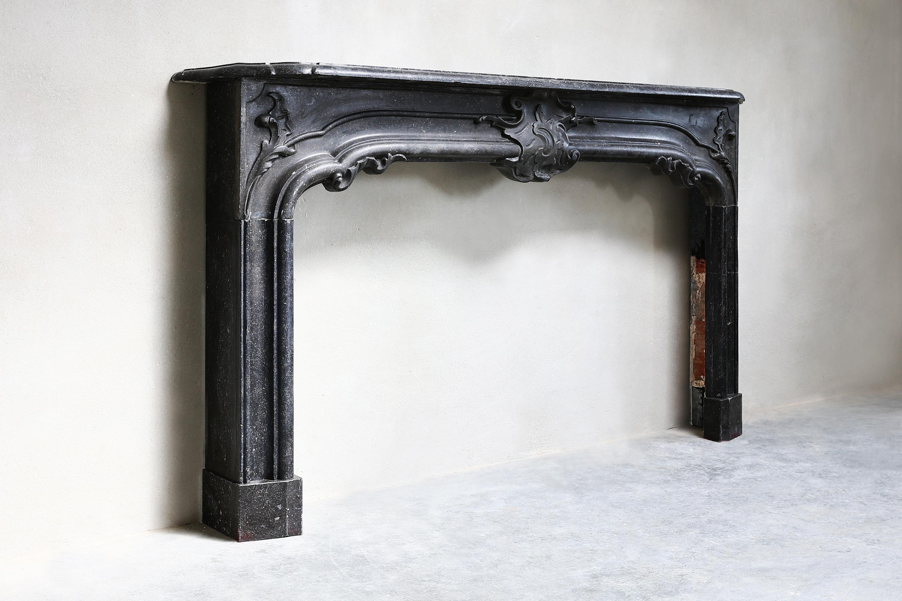 Beautifully decorated fireplace of Belgian bluestone from the 19th century with a width of no less than 208 cm. This fireplace is in the style of Louis XVI. A beautiful striking fireplace with ornaments in the middle of the front part and on the