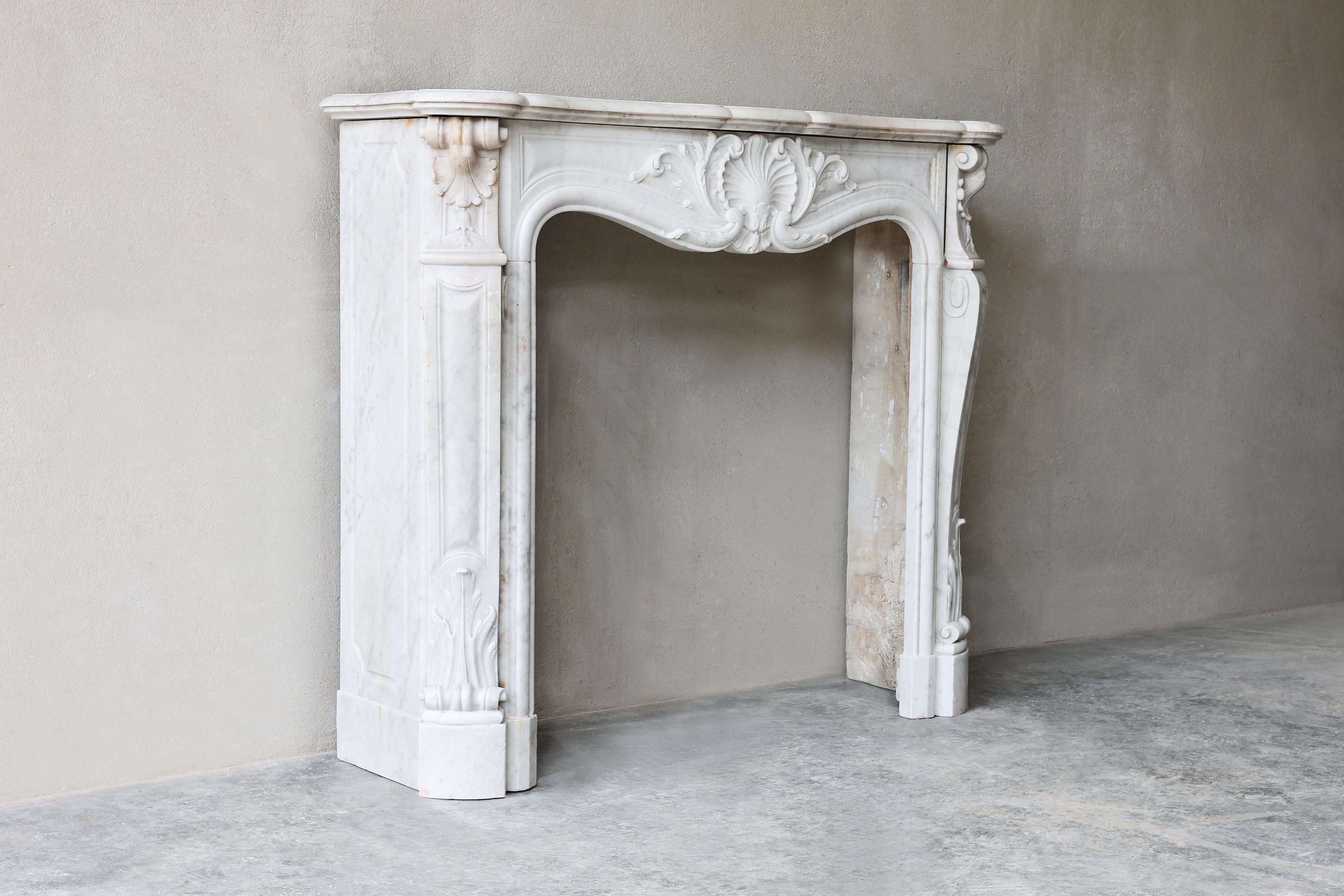 Beautiful compact and antique fireplace of Carrara marble from Italy! This fireplace is in the style of Louis XV and has 'trois coquilles', a large shell in the middle of the front part and two shells on the legs. The fireplace dates from the 19th