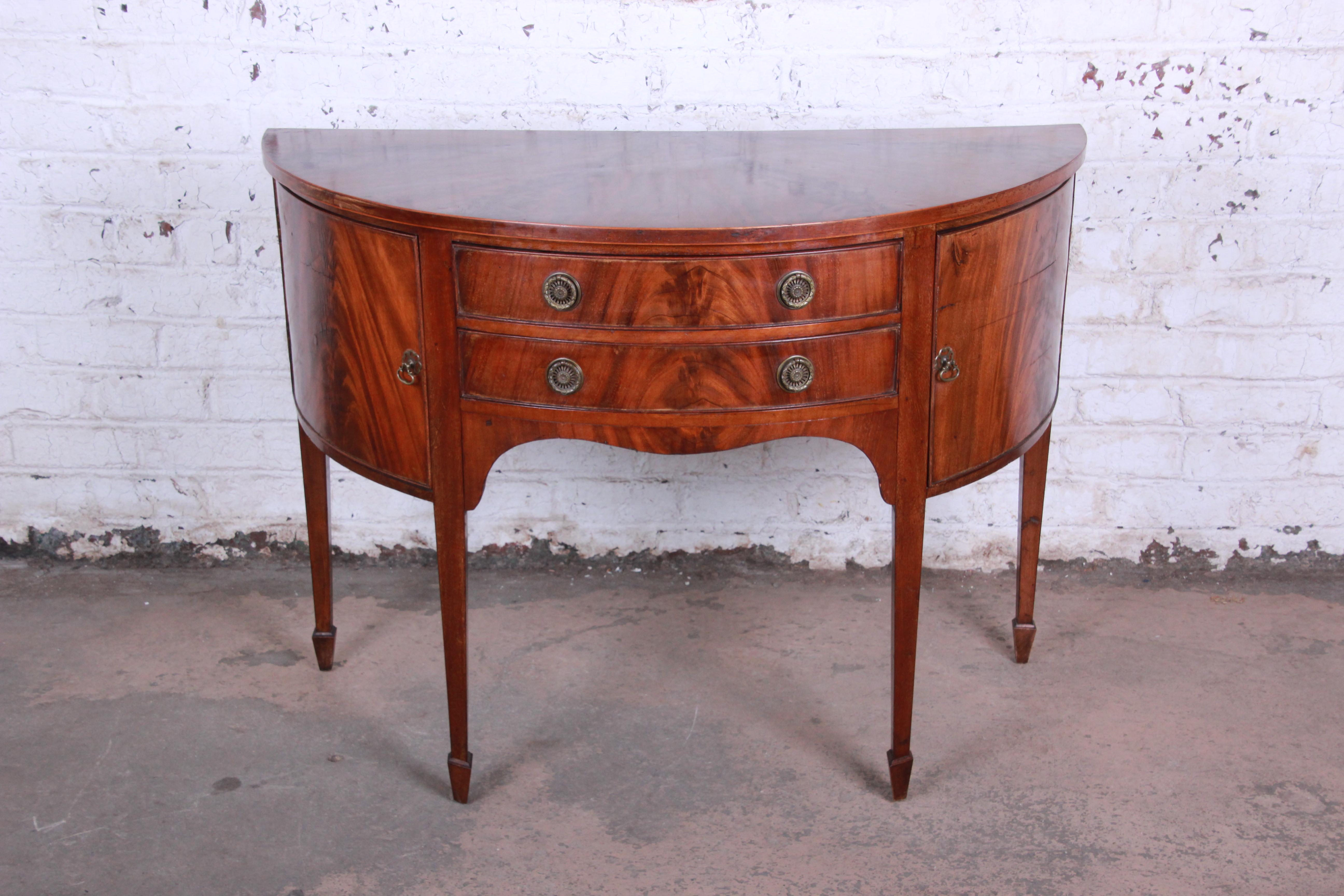 A gorgeous 19th century flame mahogany demilune sideboard cabinet. The sideboard features stunning flamed mahogany wood grain and a nice traditional style. It offers good storage, with open cabinet space behind curved doors on each end and two