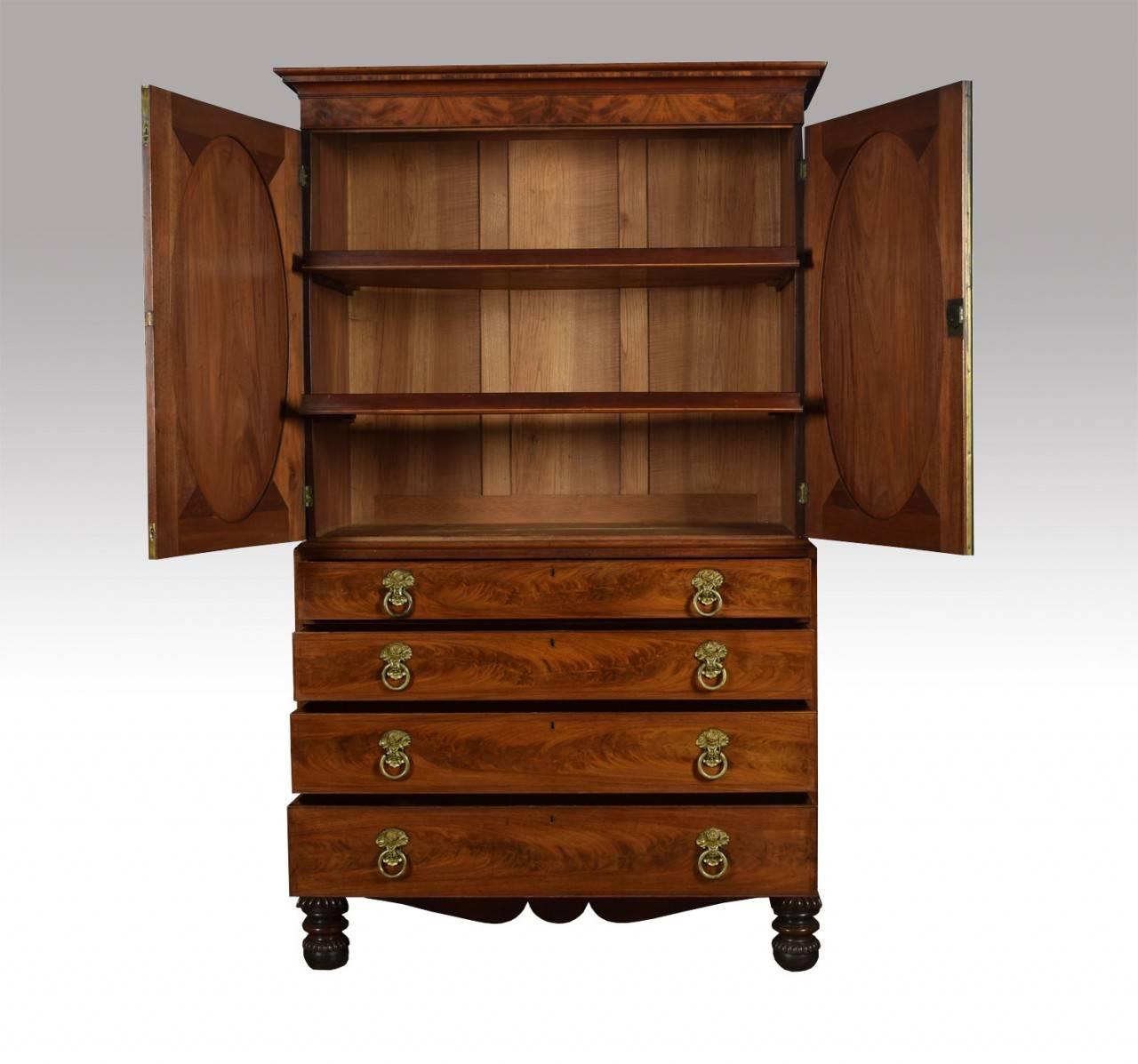 A 19th century flame mahogany press cupboard, the projecting cornice above a pair of inlaid oval panel doors opening to reveal two sliding trays. The base section fitted with four long graduated drawers with original tooled ring handles all raised