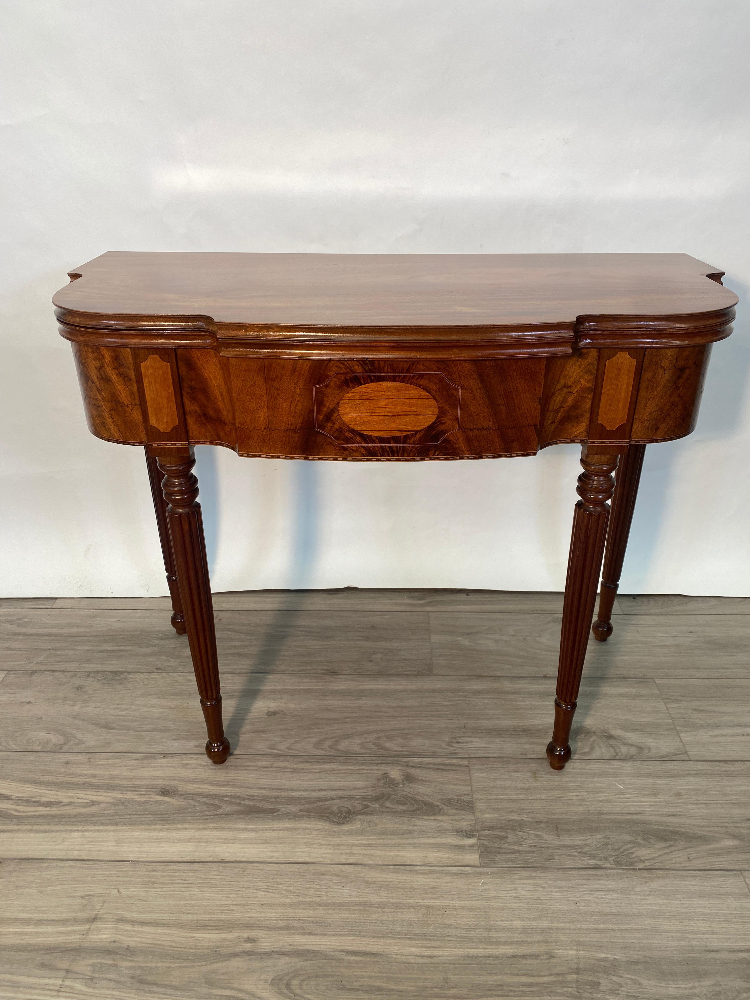 Un meraviglioso tavolino a ribalta in mogano massiccio in stile Sheraton. Una gamba del cancello sul retro si apre per sostenere la parte superiore. Splendidi grembiuli in mogano fiammato con intarsi a fasce. Quattro gambe tornite e scanalate. Da