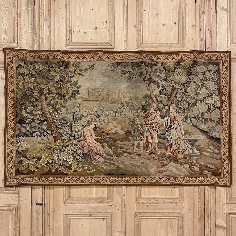 19th Century Flemish Hand-Knotted Romantic Tapestry depicts an affluent family on an outing to the grounds of their estate, with the manoir visible in the distance.  Lush greenery including a tree canopy that envelopes the scene is a sign of fertile