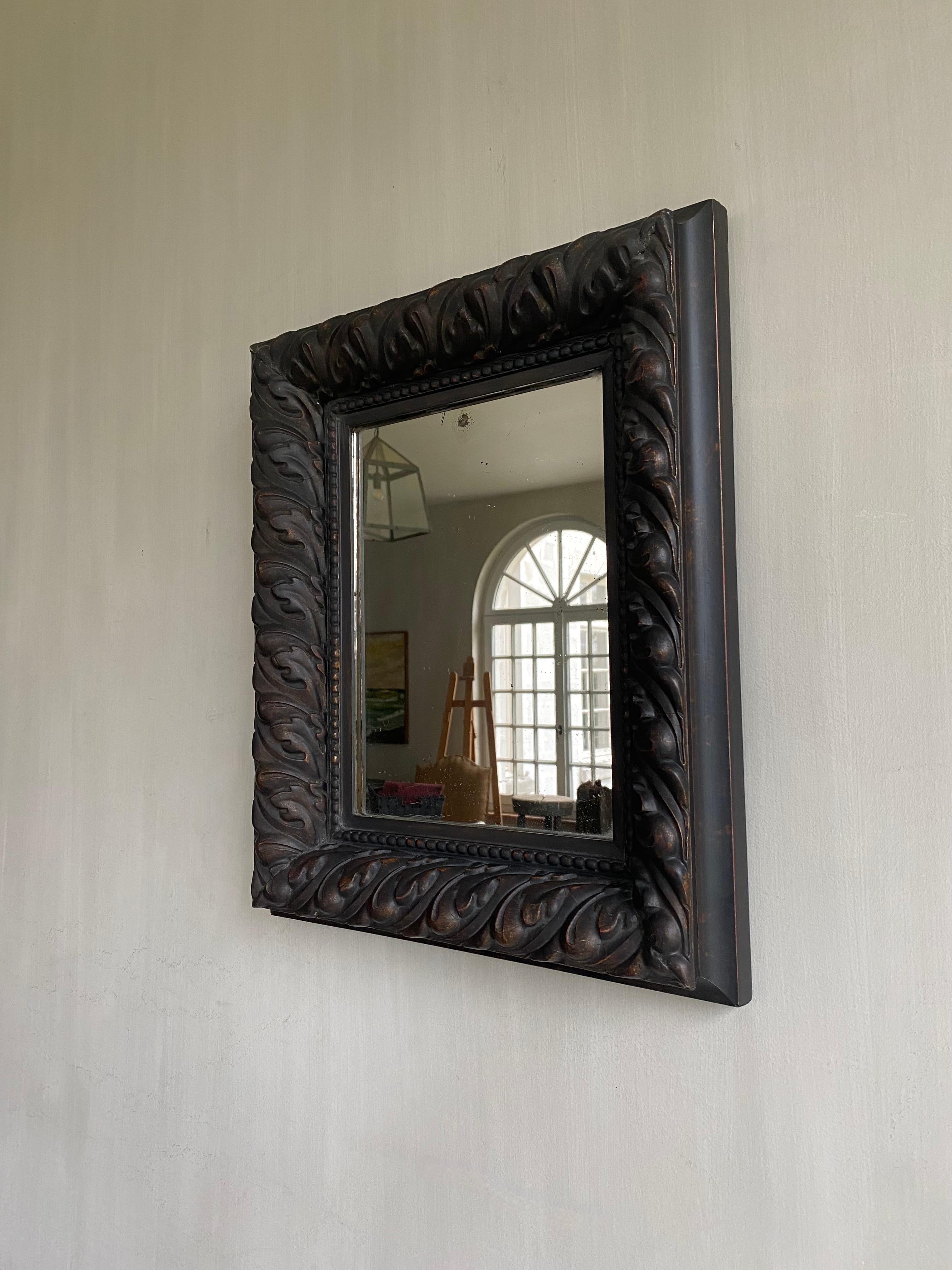 This beautiful mirror with a repetitive pattern of a lobed oak leaf has a calm and simplicity about it, despite the carvings present.
The wood is gilded and set in ebony on top.
The mirror glass has nice weathering at the back due to age. The