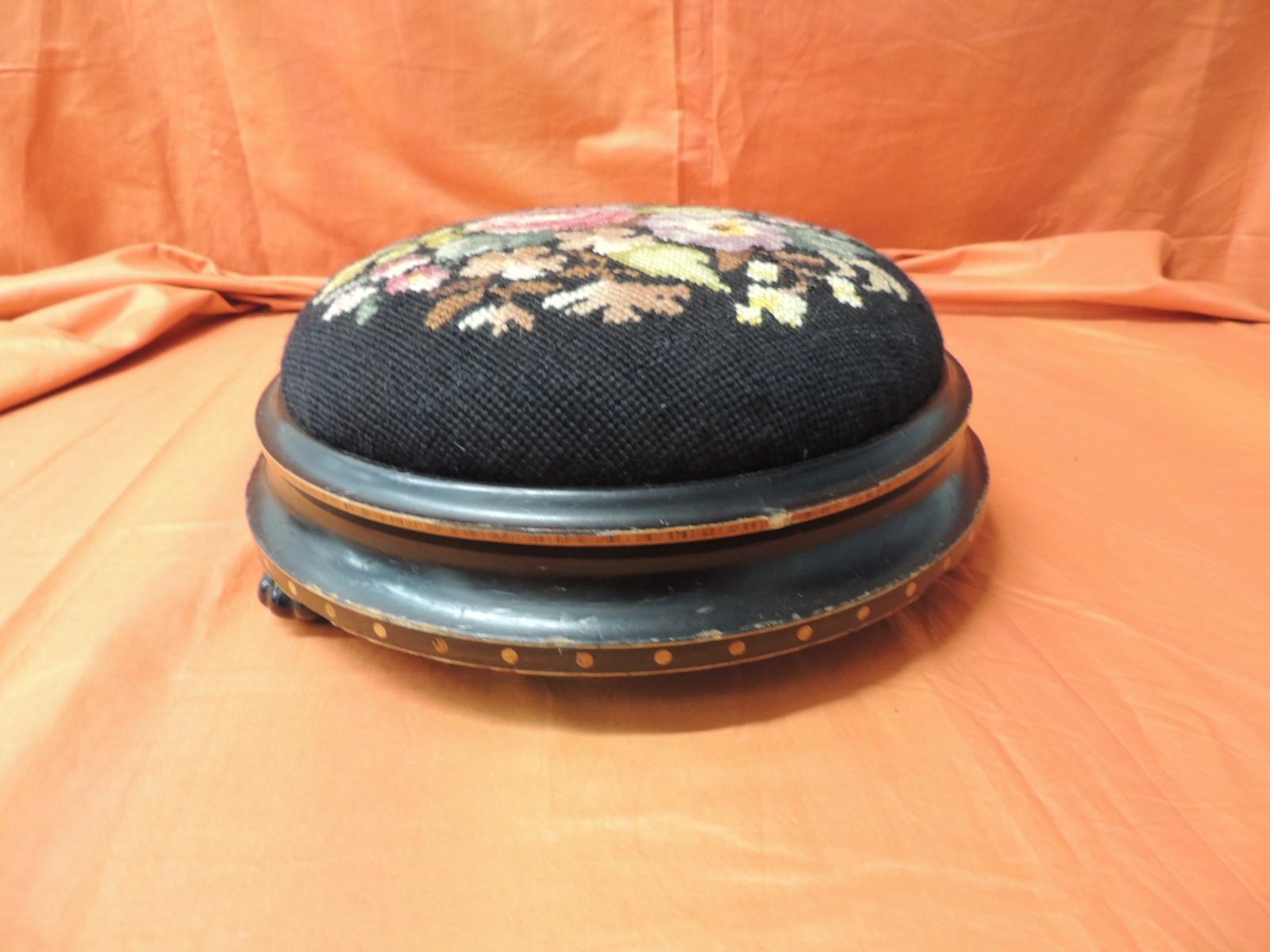 19th century English round footstool
Round footstool upholstered in a black floral tapestry. 
The ebonized wood base has inlaid all around.
Black glass feet in the shape of a flower
Size: 12 D x 4.5 H.
 