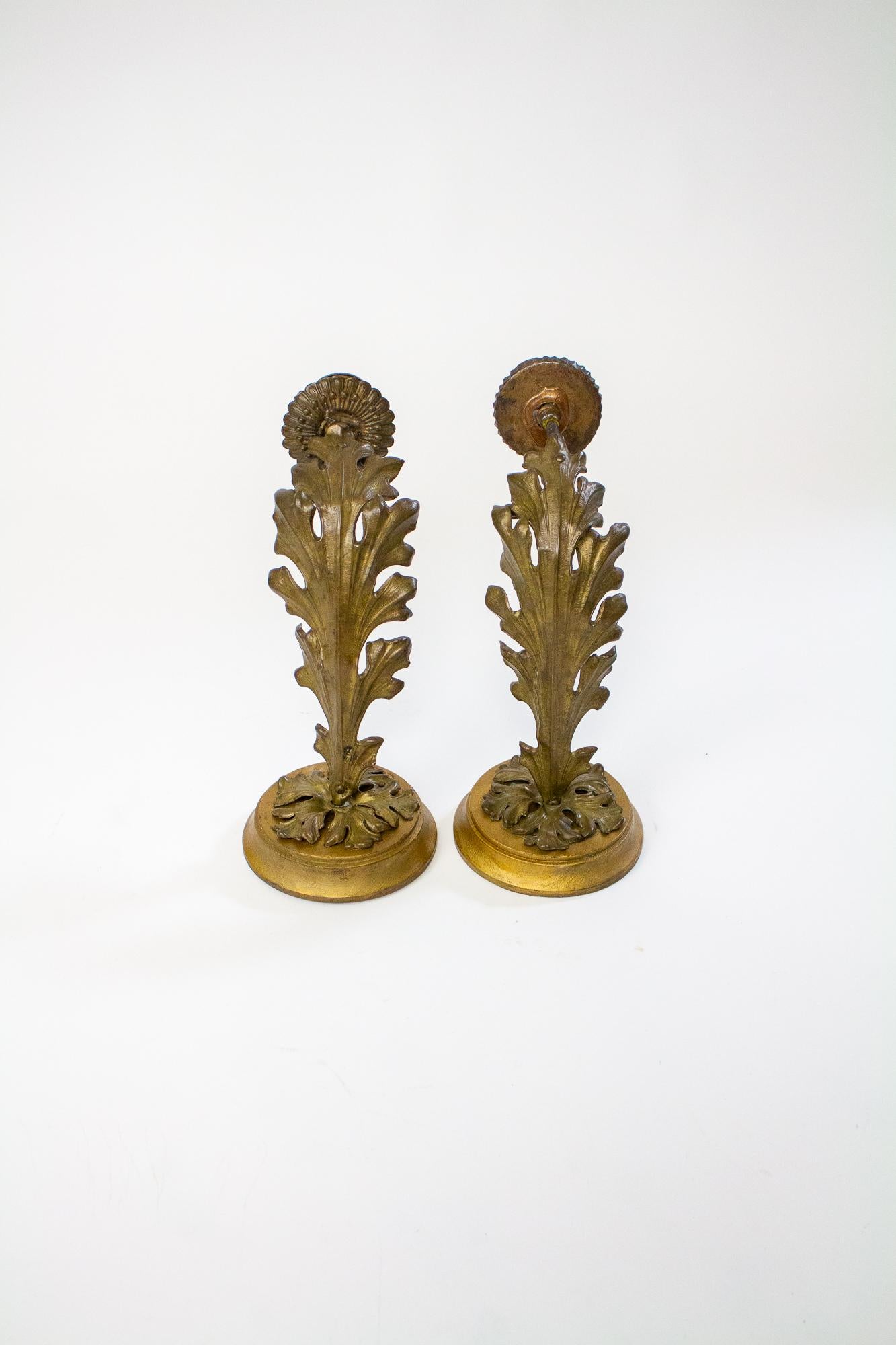 These sconces have large stamped brass leaves forming the arms, with a steel tube forming the structure. Round wooden backplates with stamped brass foliate ornaments. The bobeches are slightly different, and the candle cups are somewhat bent, but