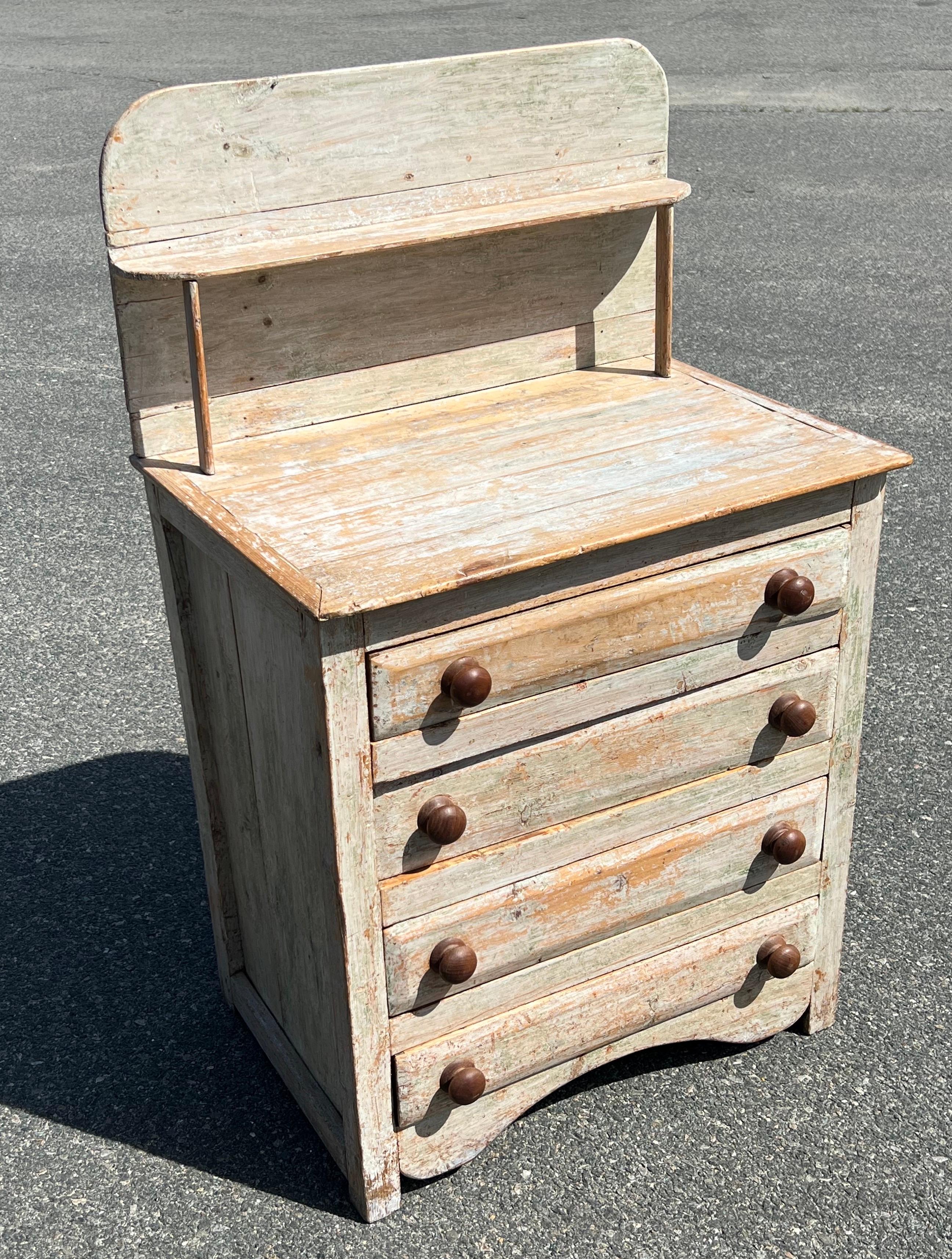 19th century 4 drawer dresser with gallery and upper shelf.  In original white over green paint and natural wooden knobs.  Smoothly operating drawers with beveled fronts, shaped toe kick, illegible signature on reverse.  Surface height 32 inches.