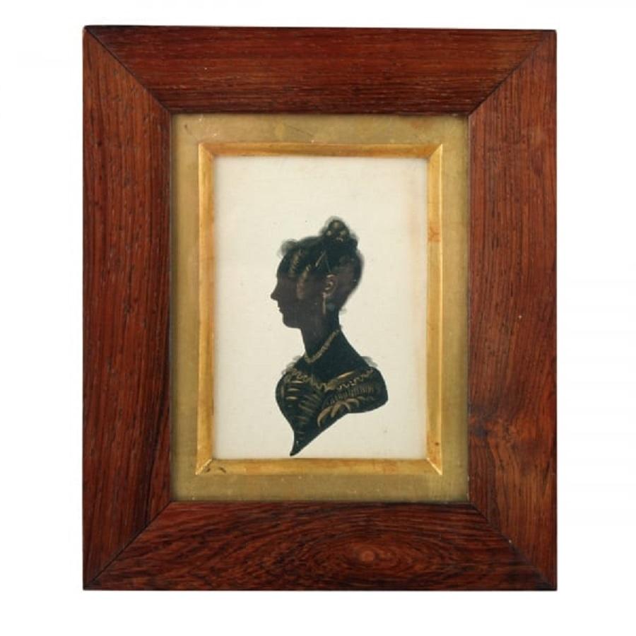 A middle of the 19th century early Victorian silhouette.

The silhouette is of a young lady wearing a dress with a lace neckline, earrings and a necklace.

The silhouette has a gilt wood slip and a rosewood veneered frame.

The silhouette and