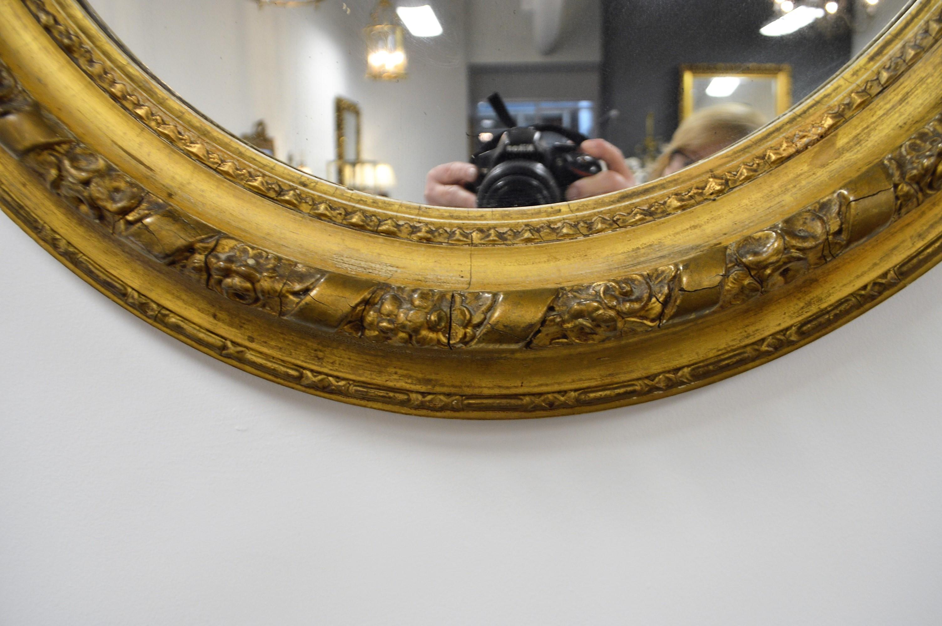 Floral and ribbon carving all around the frame of this 19th century mirror from France. The frame has had some repair but the overall condition is good. There is an nice aged patina to the leaf gilding.