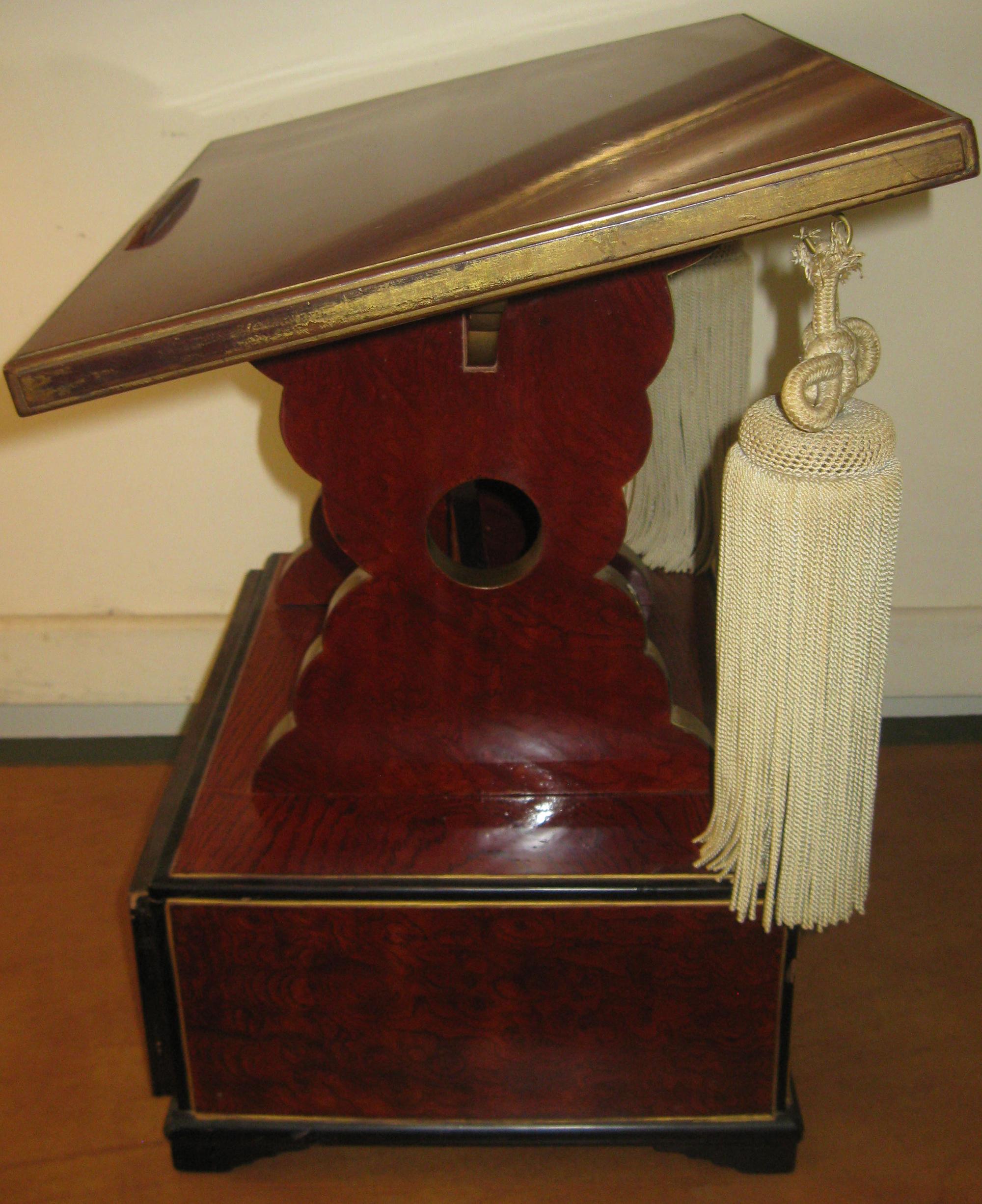 Unusual carved wooden book pedestal from a fraternal order lodge. Features include faux bois painted finish with gold and ebony highlights, slant top, bracket feet, scalloped supports and fancy silk tassels. One drawer with original brass pull. See