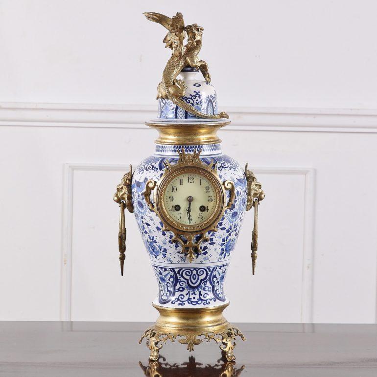 19th Century French, three-piece, porcelain-and-ormolu clock garniture set. Highly ornate brass accents on the blue and white hand-painted porcelain clock body and candleholders. Porcelain is in excellent condition. The clock is set within a lidded