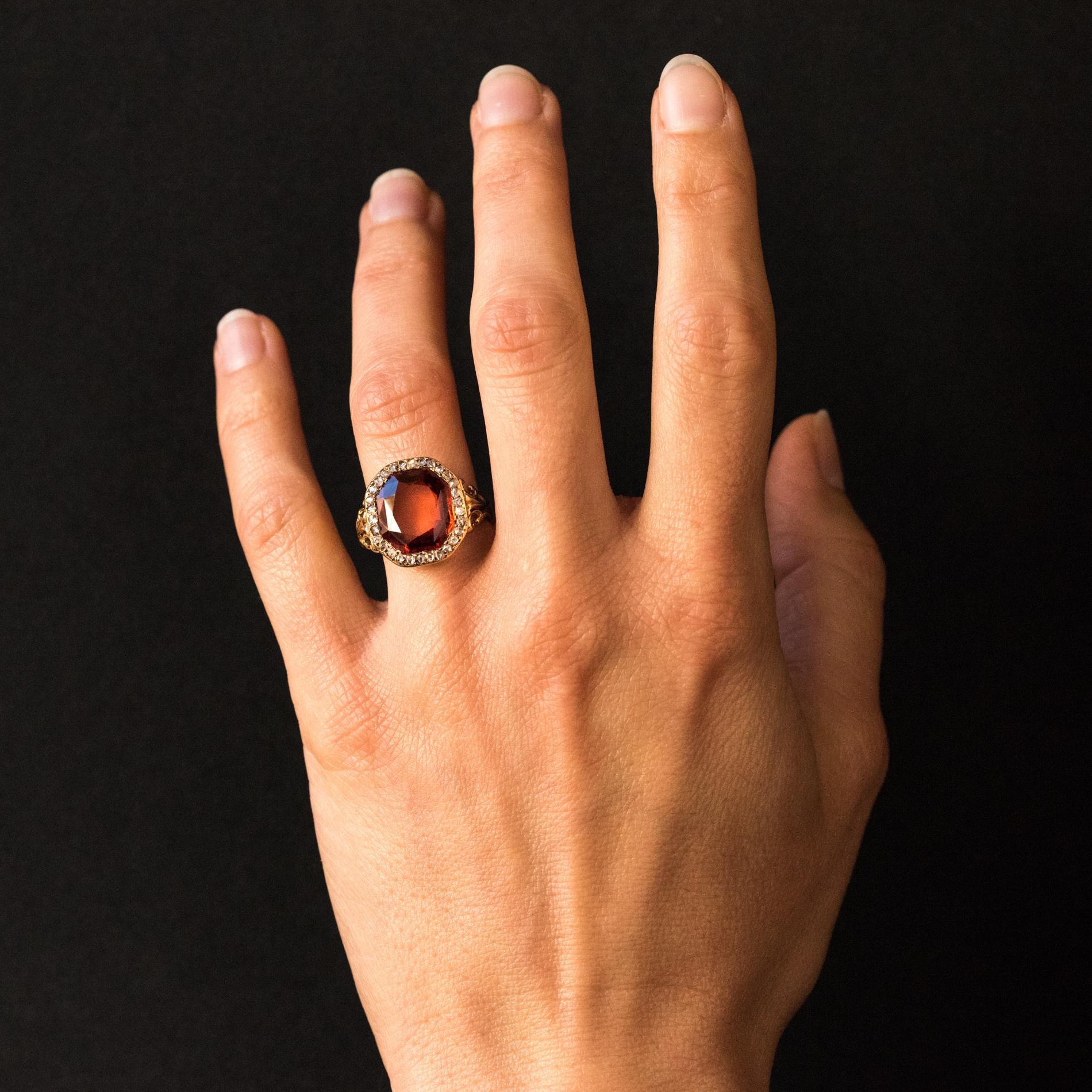 Ring in 18 carats yellow gold, eagle's head hallmark.
This beautiful ring is adorned with a hessonite orange garnet surrounded by rose-cut diamonds. On both sides, the start of the ring forms a fleur-de-lys pattern.
Total weight of garnet: 6.20