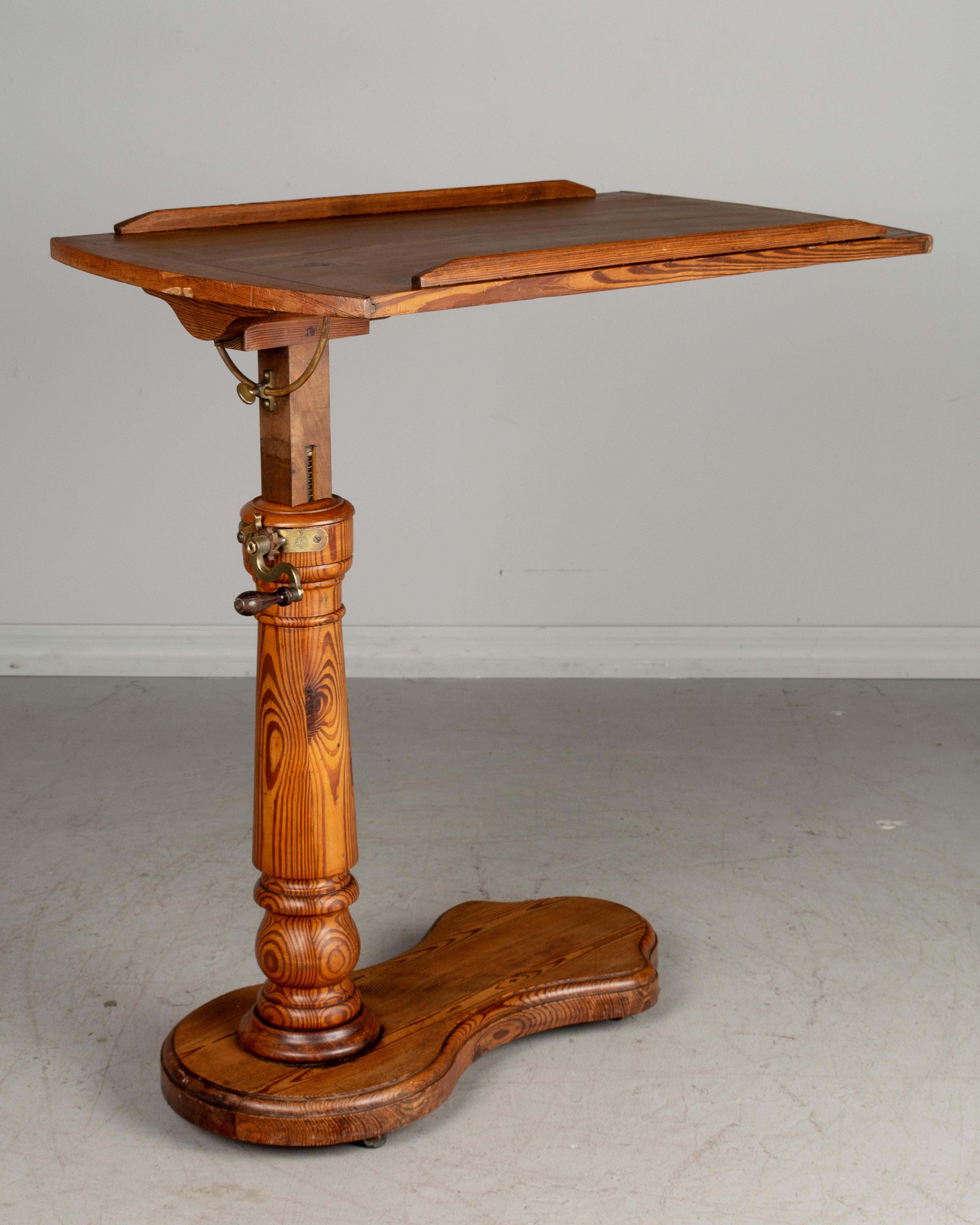 A 19th century French adjustable tilt-top tray table made of pitch pine with turned post and cast brass hardware. May be tilted flat or angled and is raised or lowered using a hand crank to a height of 32” to 45”. The base has wheels that roll
