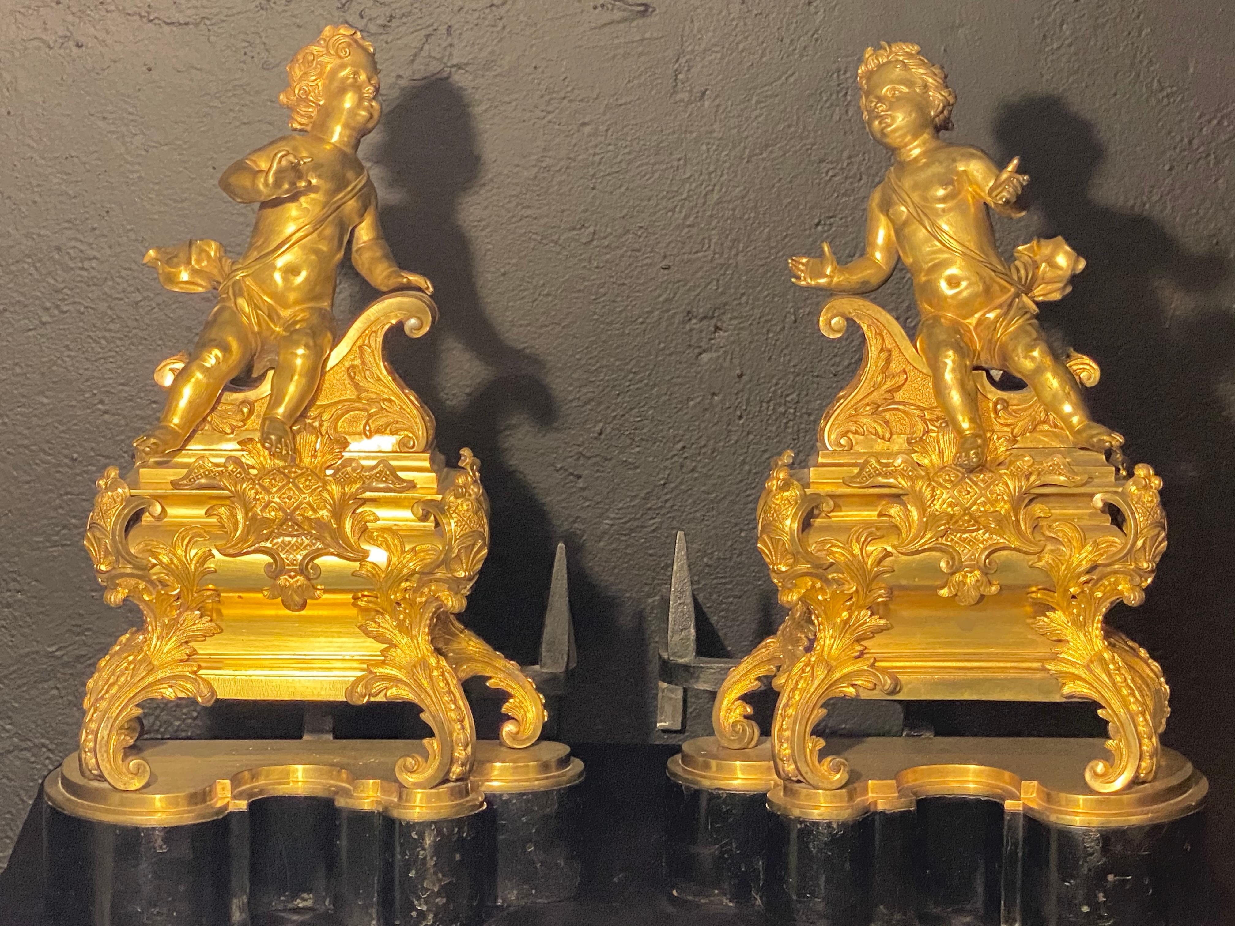 19th century French Louis XVI style Andirons. Opposing cherubs on stands in doré Bronze. This spectacular large and impressive pair of andirons are certain to spark controversy. Each having a fine doré gilt bronze finish with a pair of cherubs