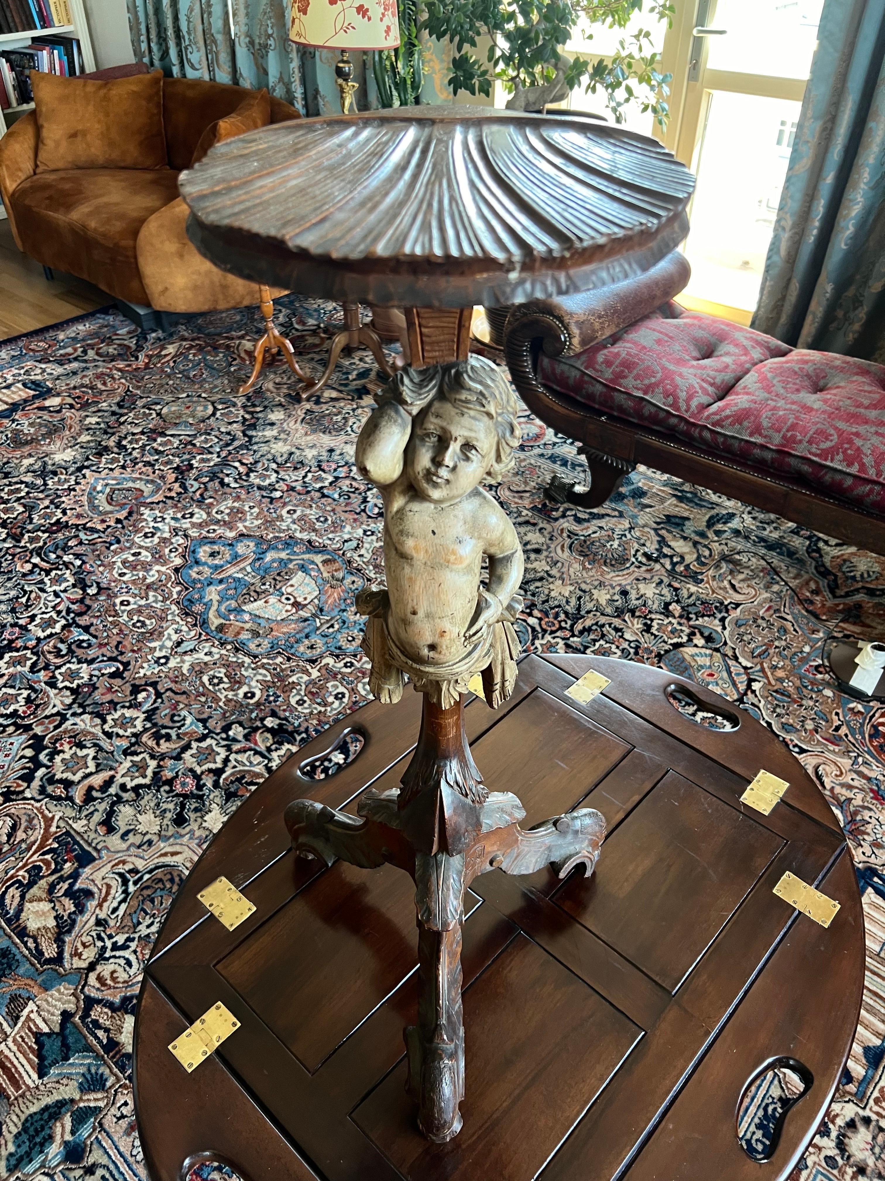Ancienne table tripode latérale française reposant sur un sabot de chèvre et trois pieds d'écurie décorés de feuilles. Au milieu de la base se trouve un chérubin délicatement sculpté et peint à la main qui tient le coquillage formé au sommet de la