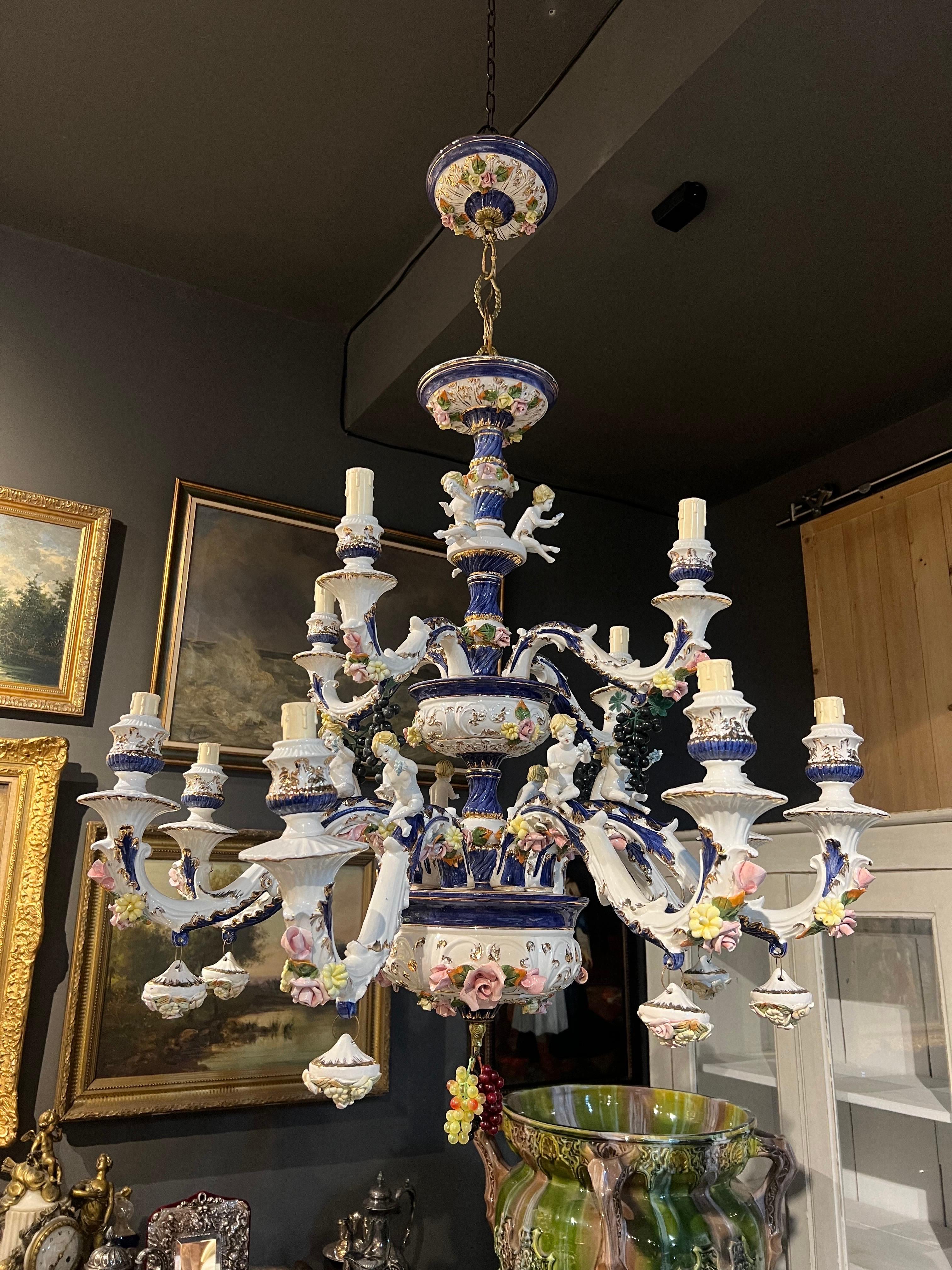 Exquis lustre français à douze bras en porcelaine faite et peinte à la main, décoré de petites roses et d'autres fleurs et de cupidons assis sur chaque bras. Très bon état authentique. Il s'agit d'une pièce étonnante qui trouvera sa place dans tous