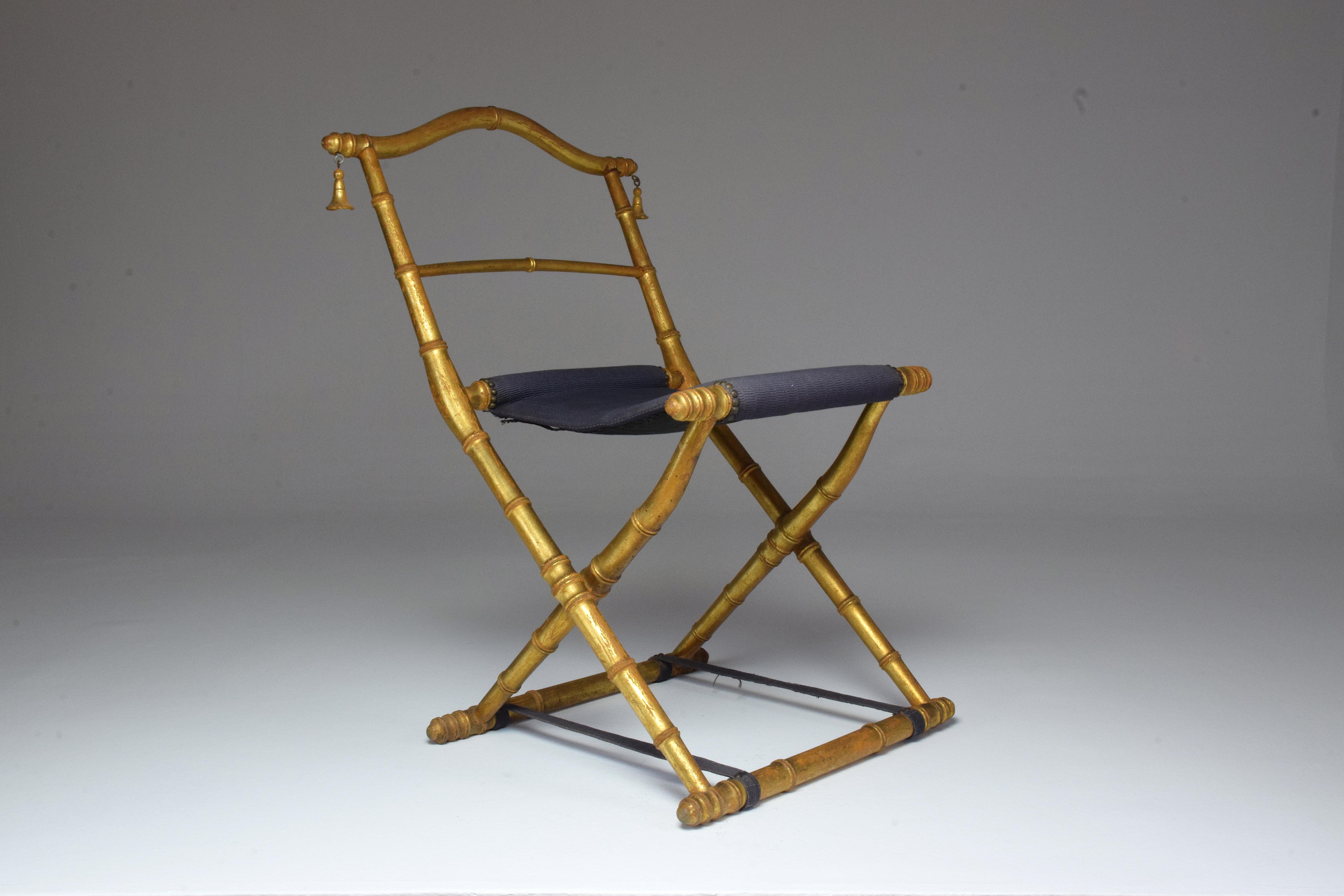 Antique children's folding chair from the 19th century Napoleon III era designed in wood sculpted in bamboo shape and covered in delicate sheets of gold. It is adorned with bells on the sides of the backrest. In its original upholstery with nailhead