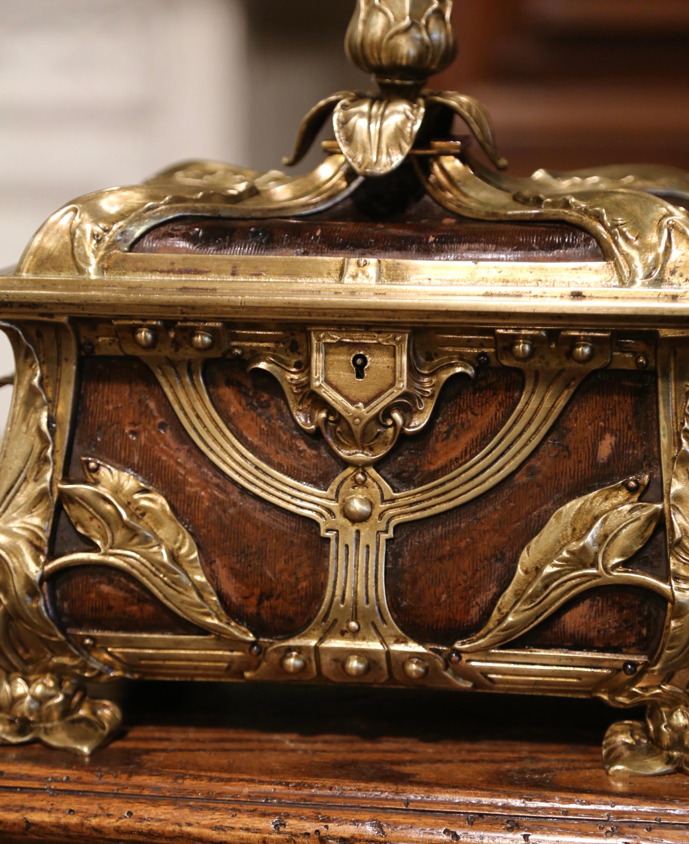 This antique casket was created in France, circa 1880. Rectangular in shape and resting on flower form feet, the gilt bronze box is dressed with a floral finial at the top. The Art Nouveau casket with bombe sides features ormulu leaf decor over red
