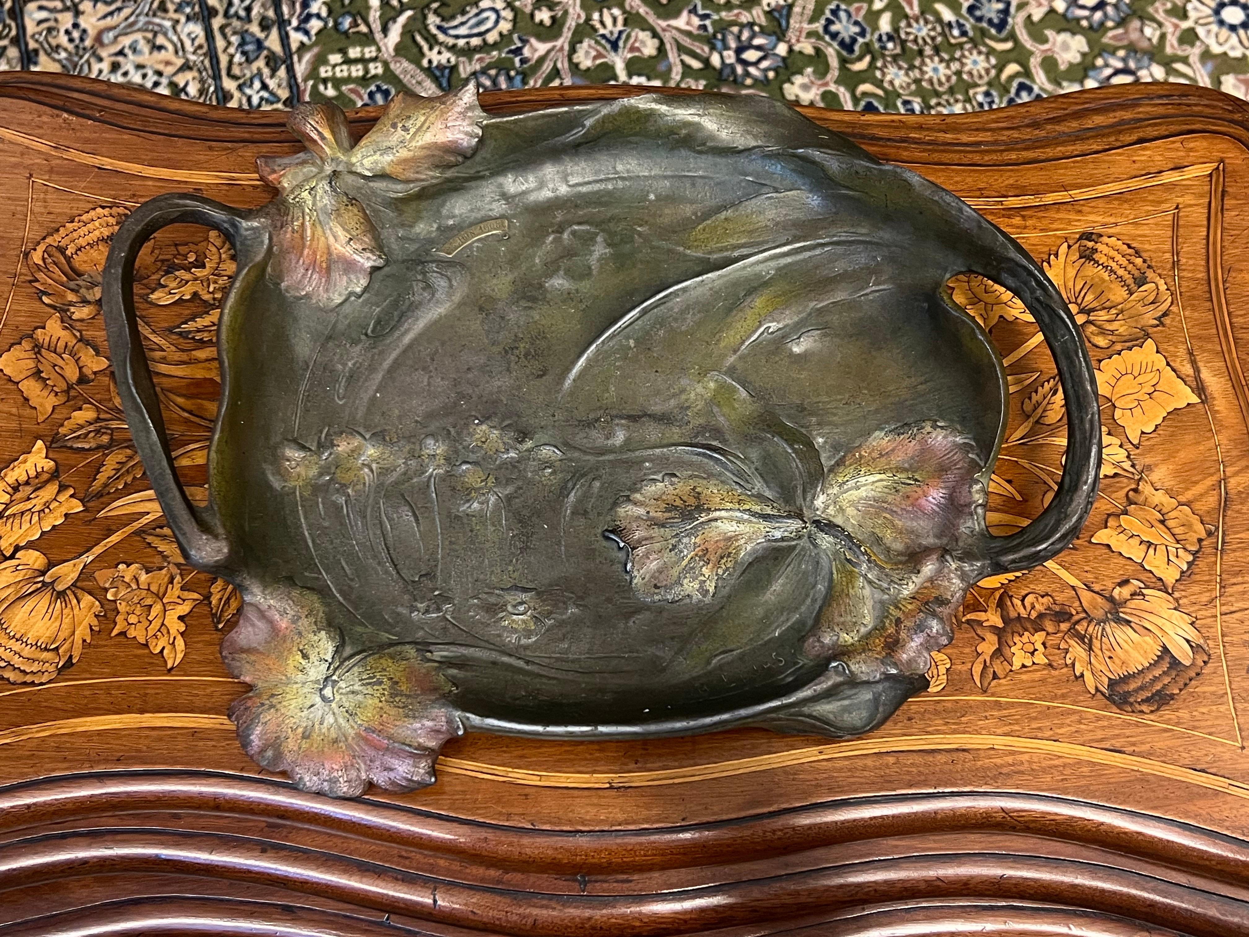 Frühes Jugendstil-Bronzetablett mit Griffen und Blumendekor, signiert von Elias.
Das Design ist sehr typisch für den Jugendstil, mit bunten Blumen und Blättern, die den Sockel umgeben. Die gealterte Patina des Stücks verleiht ihm eine sehr