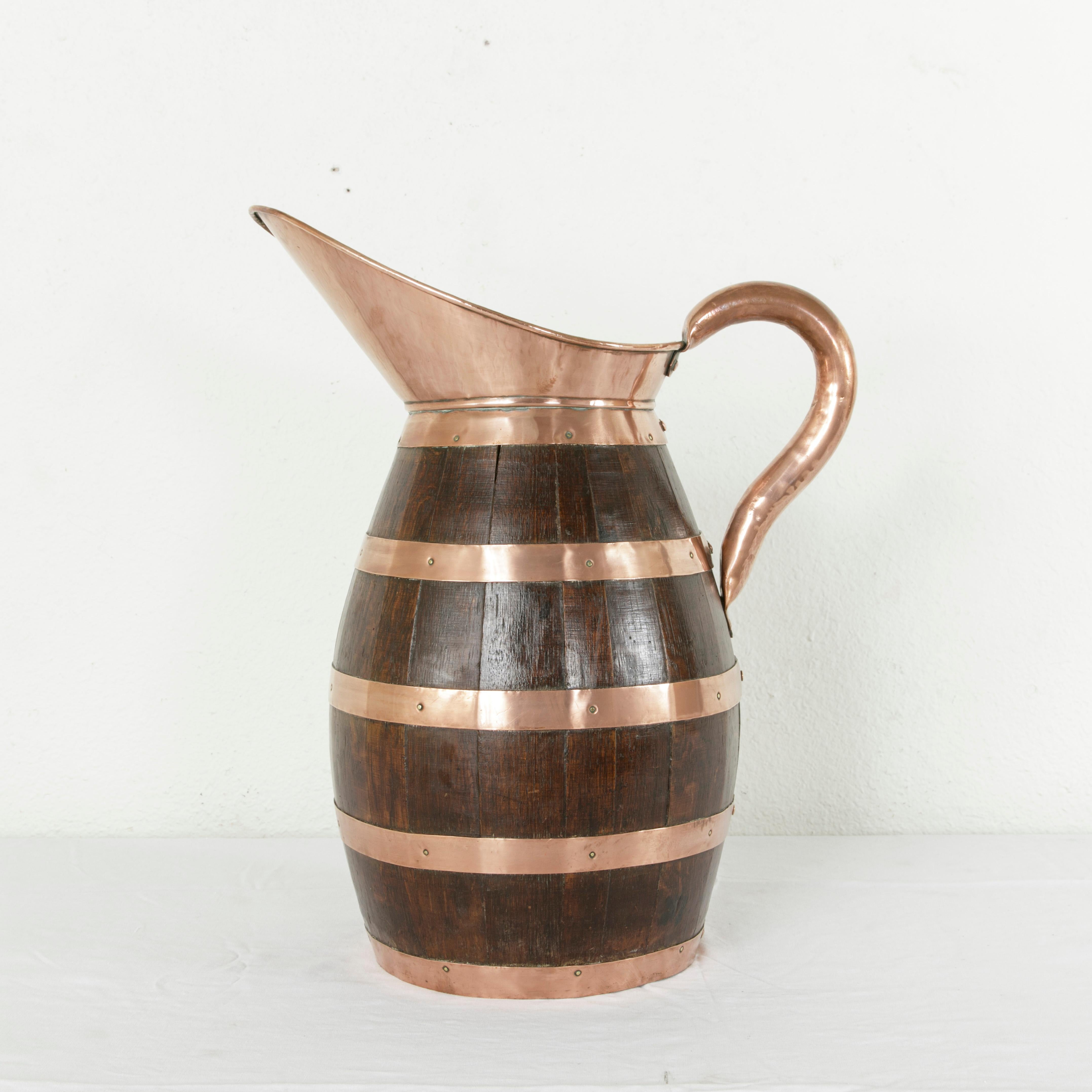 Standing at an impressive 22 inches in height, this very large late 19th century oak cider pitcher from Normandy, France, features riveted copper banding and a copper spout and handle. Artisan-made by a barrel maker, this pitcher was originally used