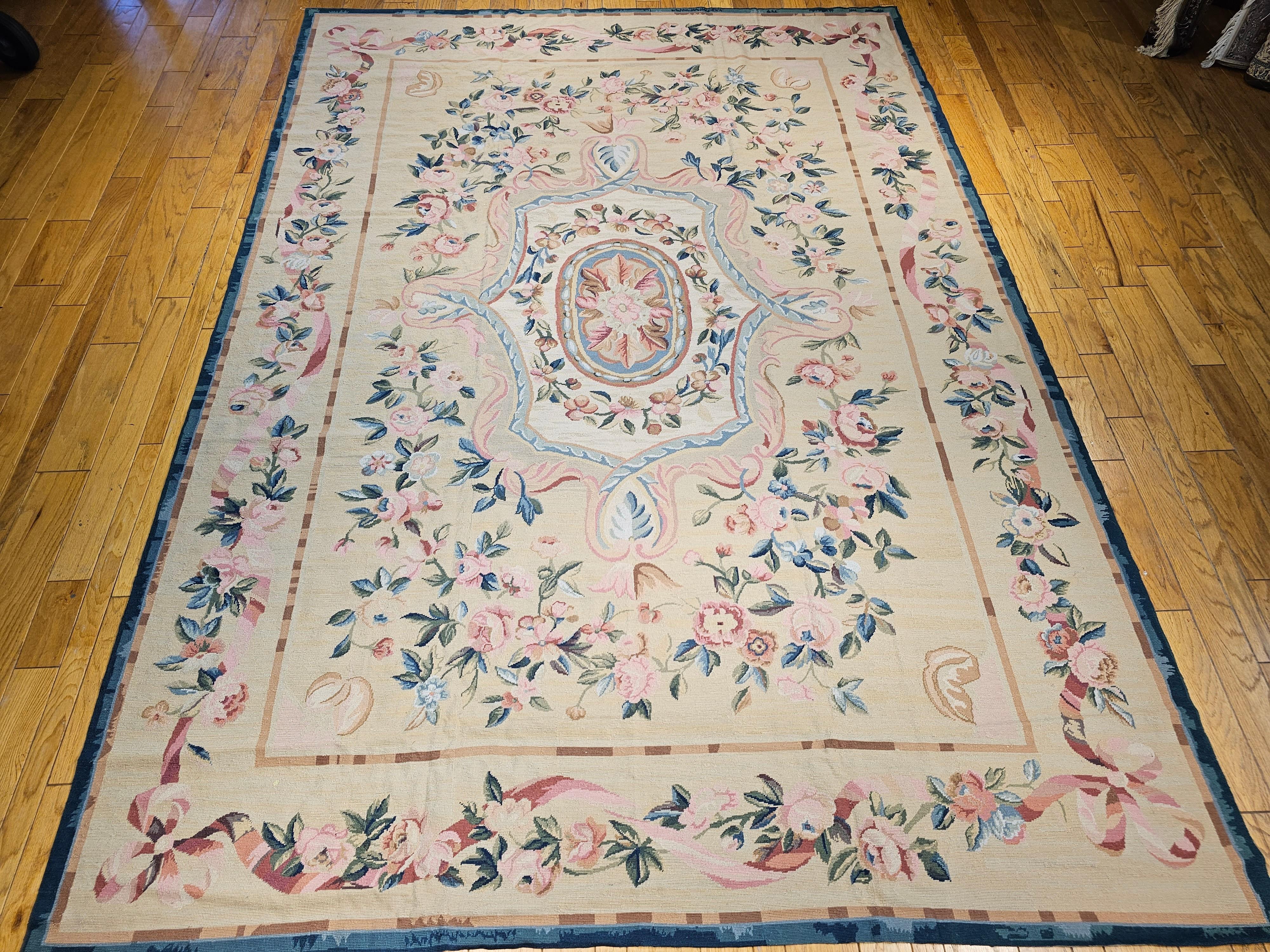 A handwoven antique French Aubusson needlework carpet from the late 1800s.  This needlepoint Aubusson rug has a floral design of large flowers and leaves in several shades of pink, red, green, brown, and gray colors set in a light yellow or beige