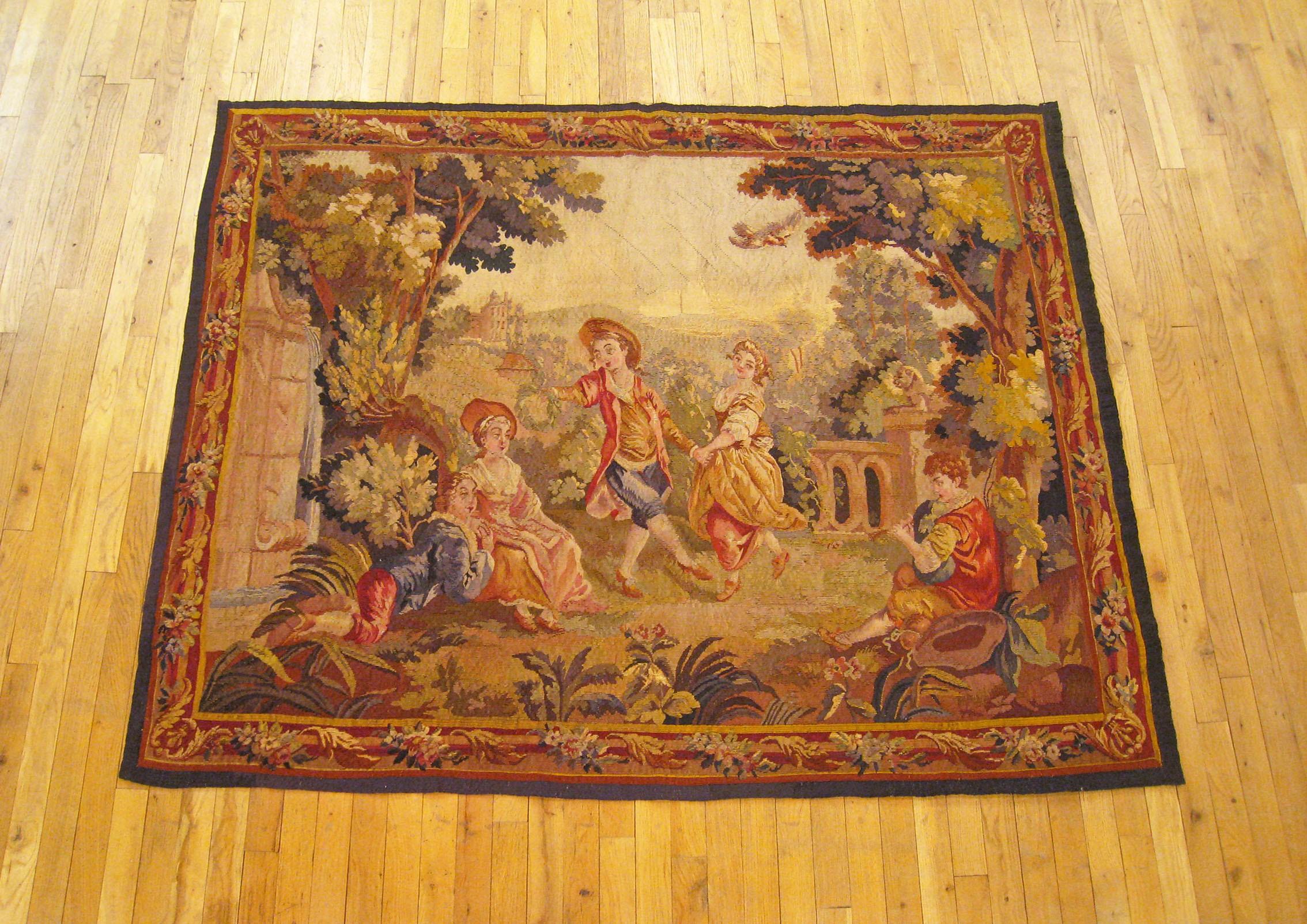 A French Aubusson tapestry from the 19th century, depicting several young courtiers spending a leisurely afternoon gaily dancing and carousing within the splendidly maintained verdant palatial grounds. Within a winding border of flower and acanthus