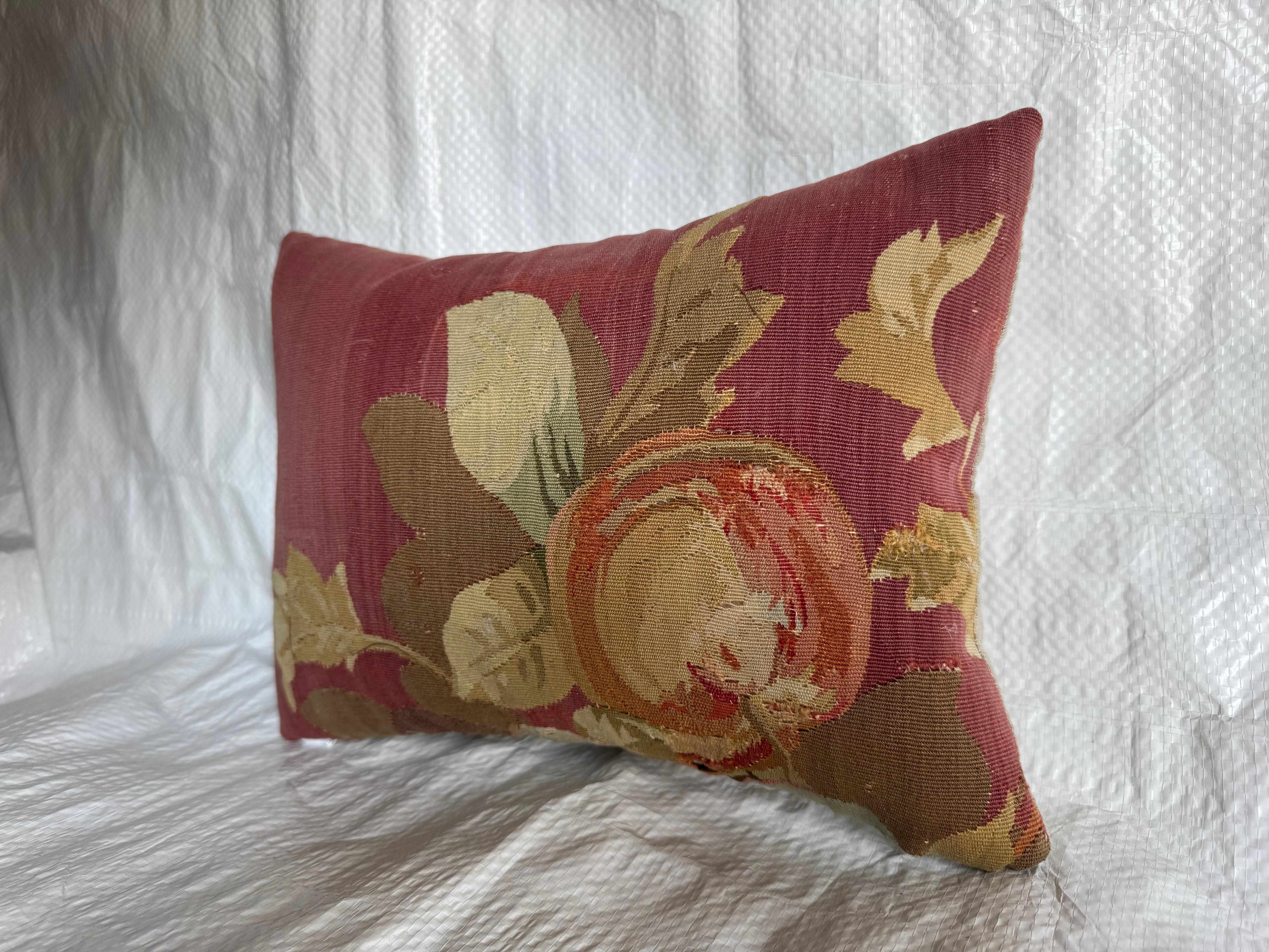 Ce coussin est fabriqué à partir d'un fragment de tapisserie d'Aubusson du milieu du XIXe siècle, datant d'environ 1850. La composition est centrée sur un motif pictural de fruit entouré de feuillage, rendu dans des tons d'ocre, d'ivoire et de vert