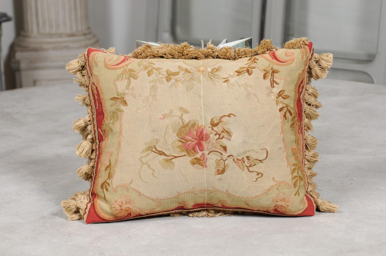 A French Aubusson tapestry pillow from the 19th century, with floral decor, foliage and small tassels. Created during the 19th century in the Aubusson tapestry manufacture located in central France, this horizontal pillow is adorned with a central