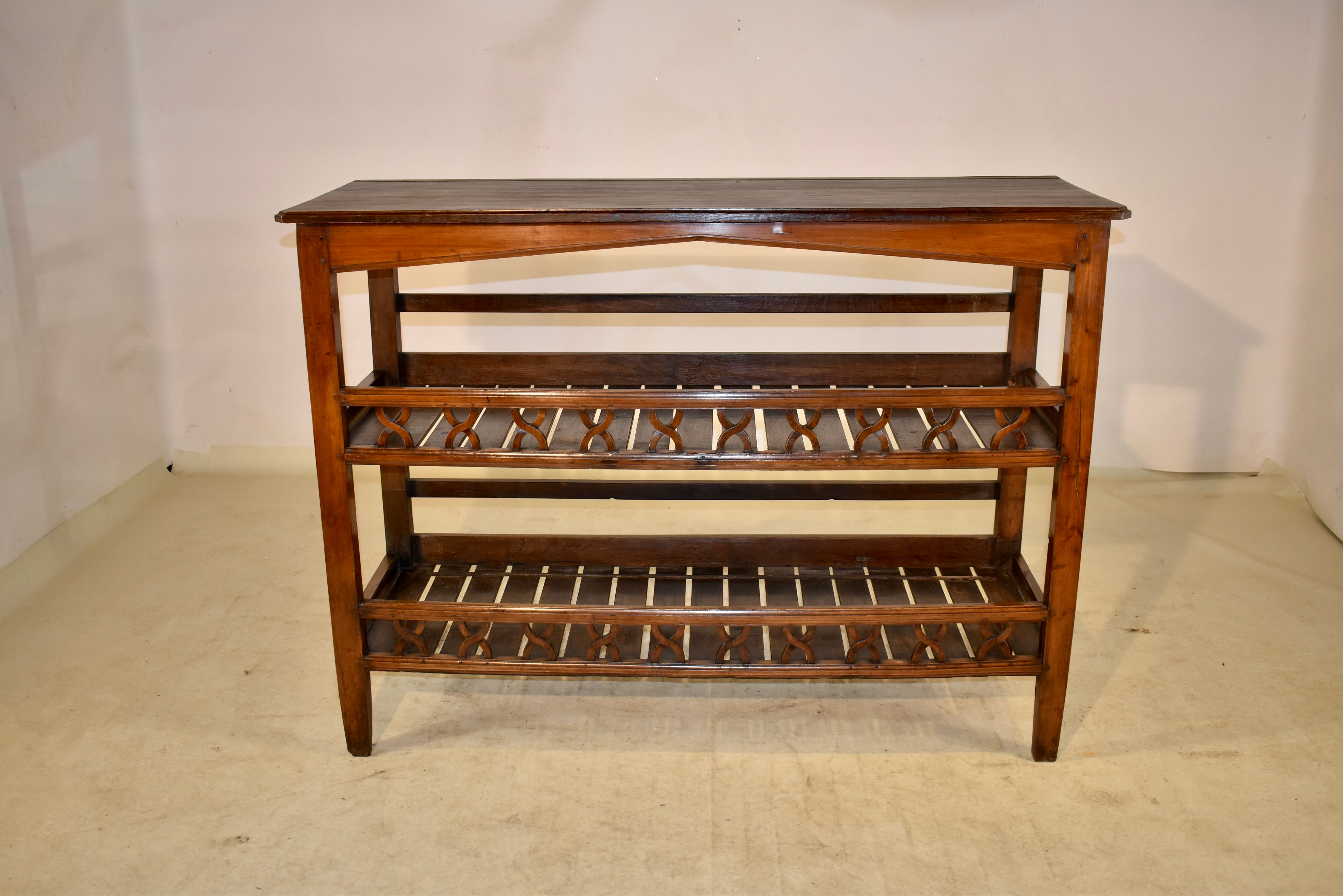 19th century oak baker's rack from France. This is a wonderful and rare piece with a beveled edge around the top following down to a simple arched apron.  There are two shelves with galleries around each side and lovely hand carved baluster-type