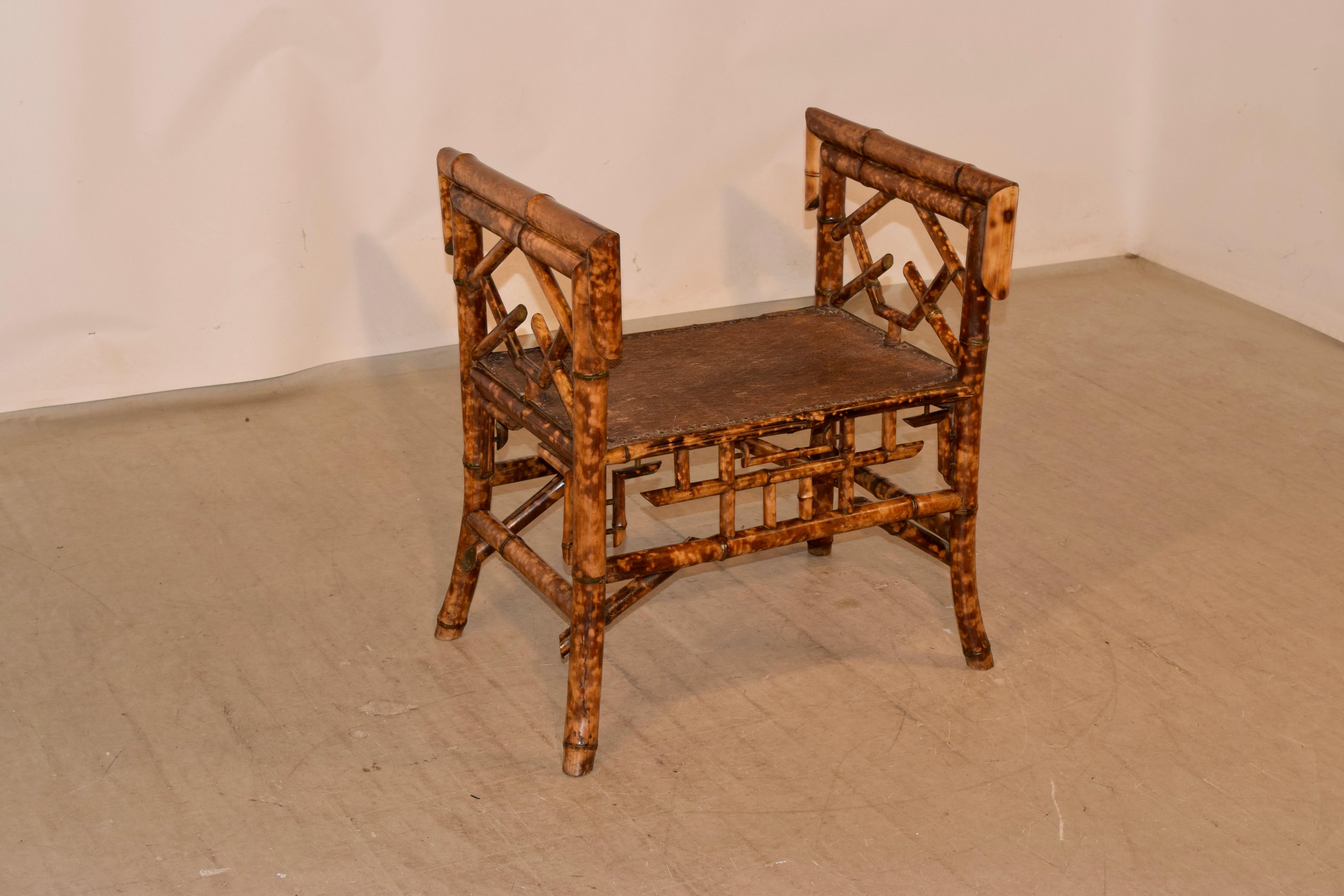 Late 19th century tortoise bamboo bench with arms from France. The arms are made from thick bamboo and are decorated in a Chinese Chippendale pattern, along with the aprons on the front and back of the bench. The seat is made from the original rush,