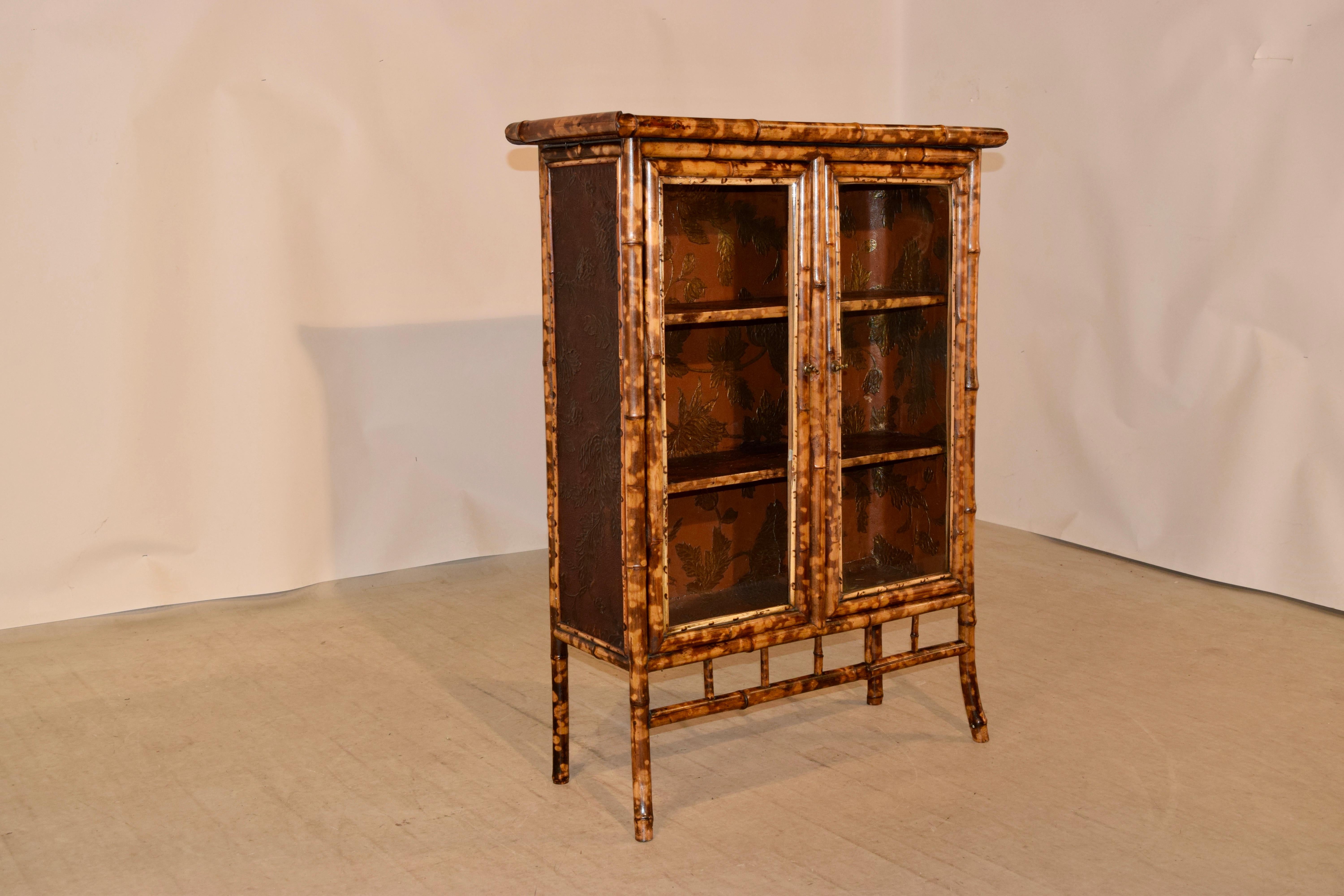 19th century French bookcase made from tortoise bamboo and pine. The top appears to be banded and have a central chinoiserie scene with a bird. This follows down to two glazed doors which open to reveal shelving. The interior is covered in antique