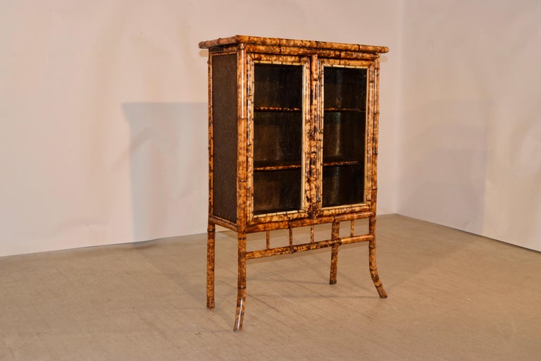 19th century French bookcase made from tortoise bamboo and pine. The top is covered with painted embossed wallpaper which has losses from age. There are two glazed doors which open to reveal shelving. The interior is covered in painted antique