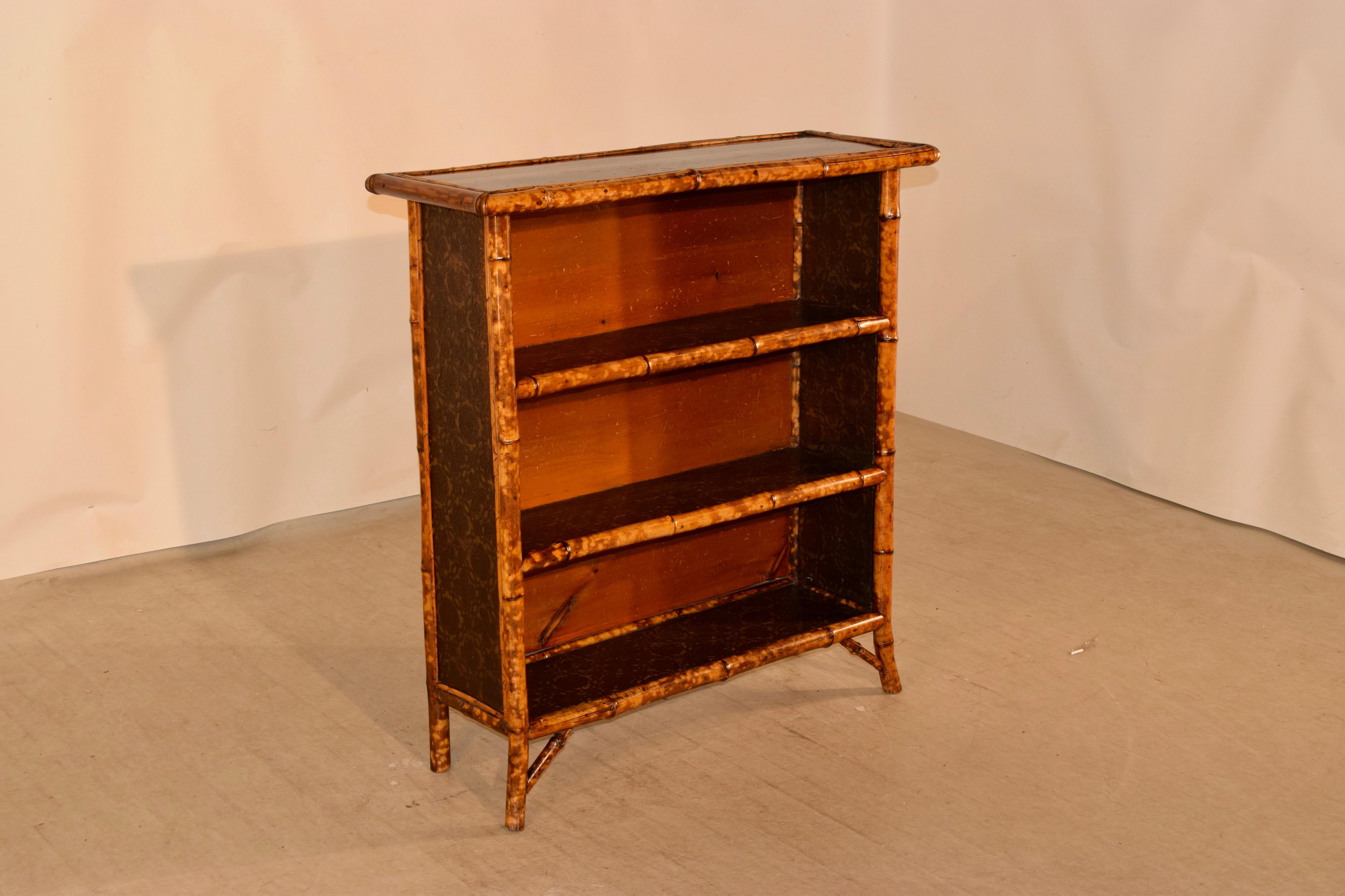 19th century bamboo bookcase from France with a chinoiserie top and three shelves, all which are covered in hand painted wallpaper, along with the sides. The case has a wooden back, and the case is raised on bamboo legs.