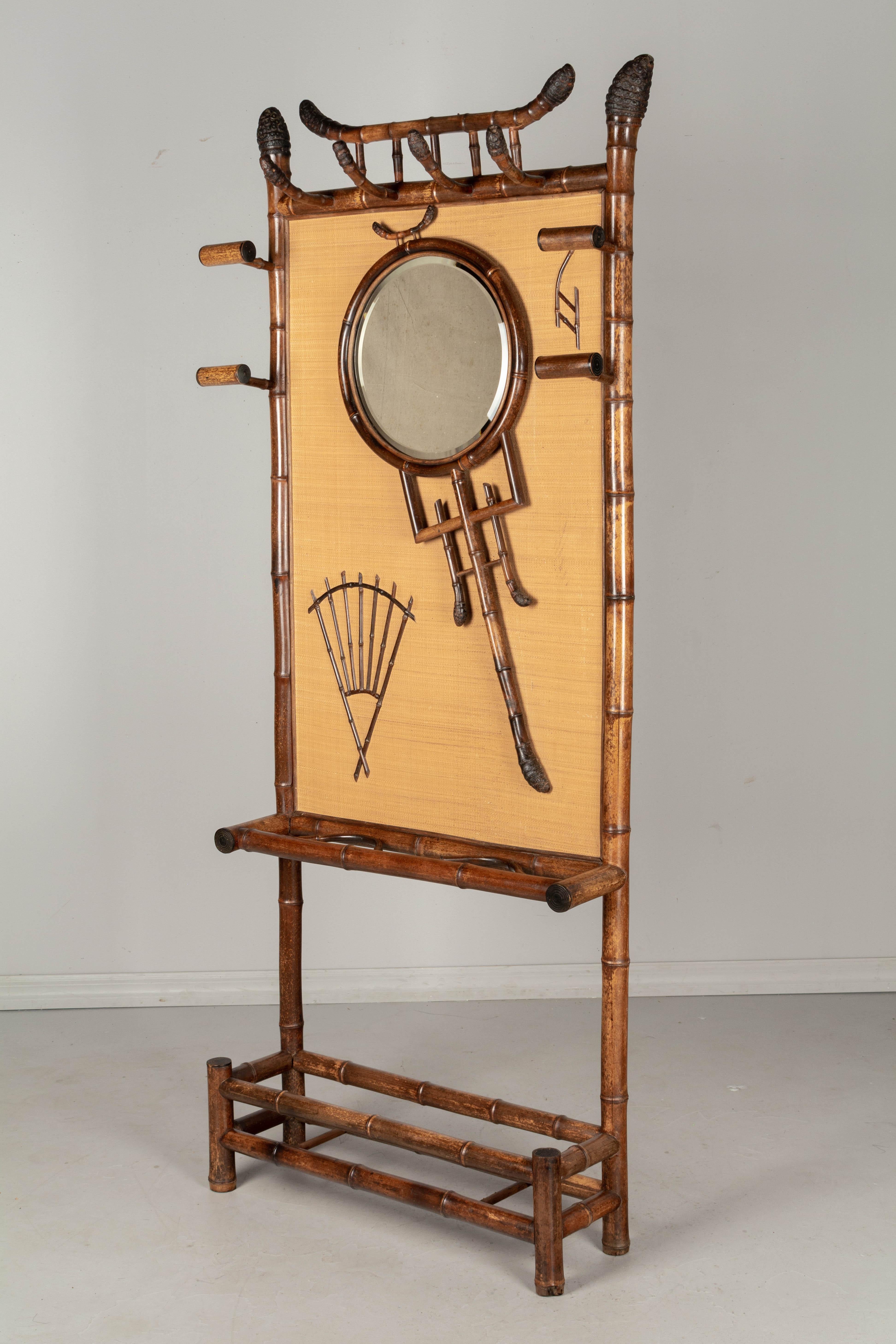 A 19th century French bamboo hall tree, or coat rack, of Japonisme design, with a circular beveled mirror and decorative elements attached to a woven back panel. Four hooks at the top are made from the root end of the bamboo shoot, as are the