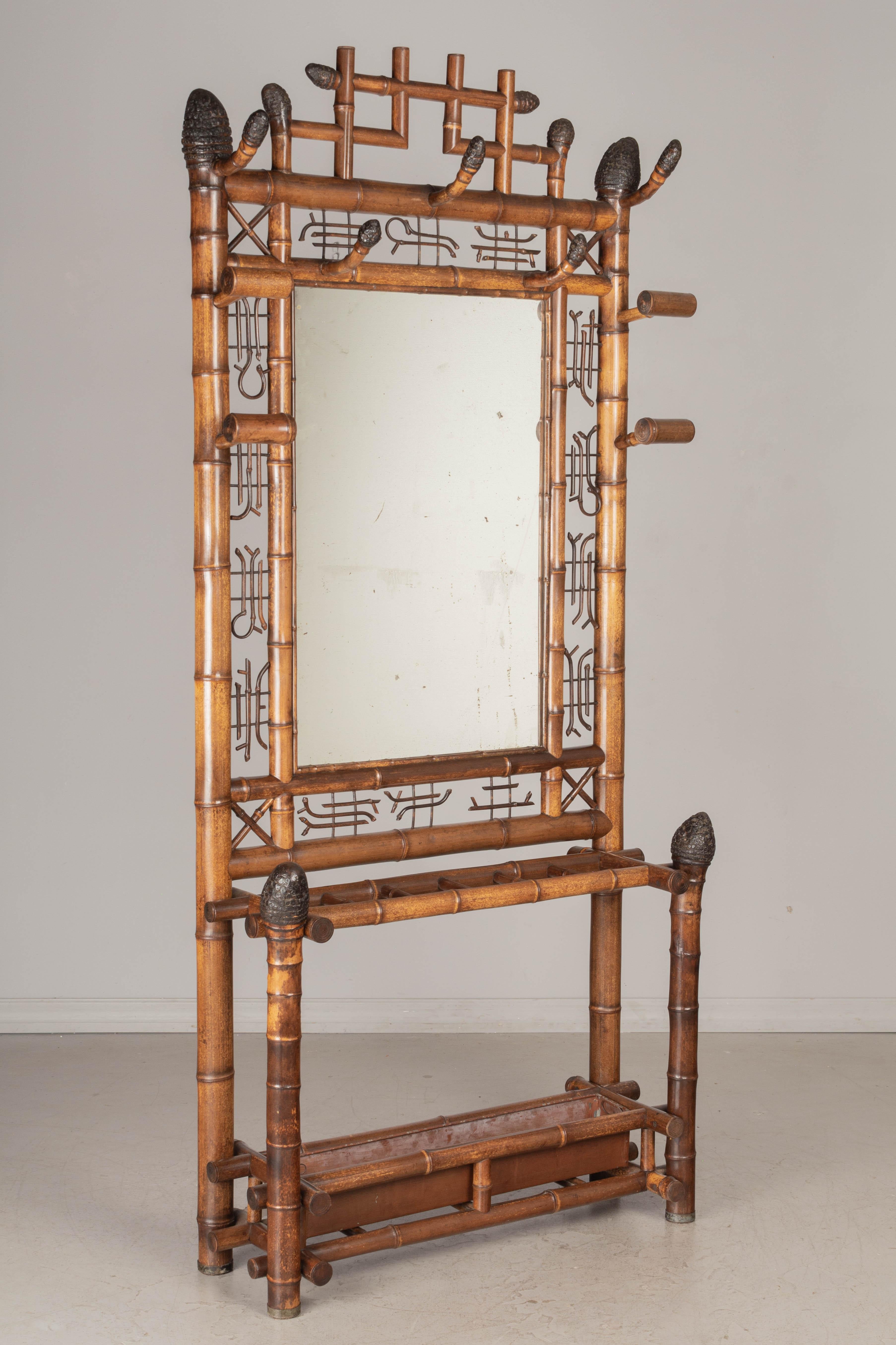 A 19th century French bamboo hall tree with a large mirror surrounded by a wide decorative border. Nine hooks for coats and hats, and an umbrella rack with removable tin drip tray. Large finials at the top and bottom made from burnt root end of