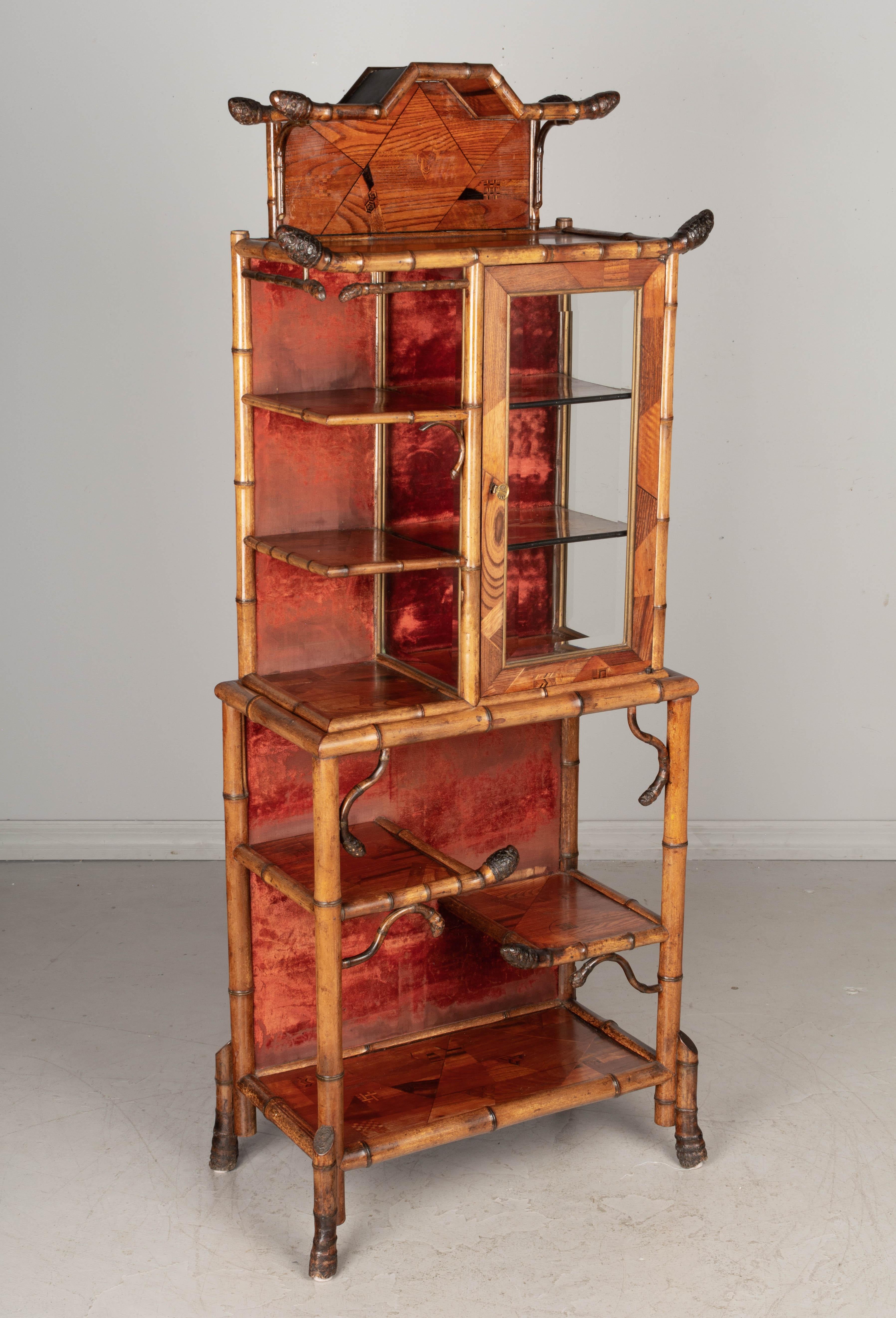A 19th century French bamboo etagere with asymmetric openwork bamboo shelves and a beveled glass paned cabinet with working lock and key. Back panel is lined in the original red velvet fabric, worn in places. Pagoda style crown with large finials