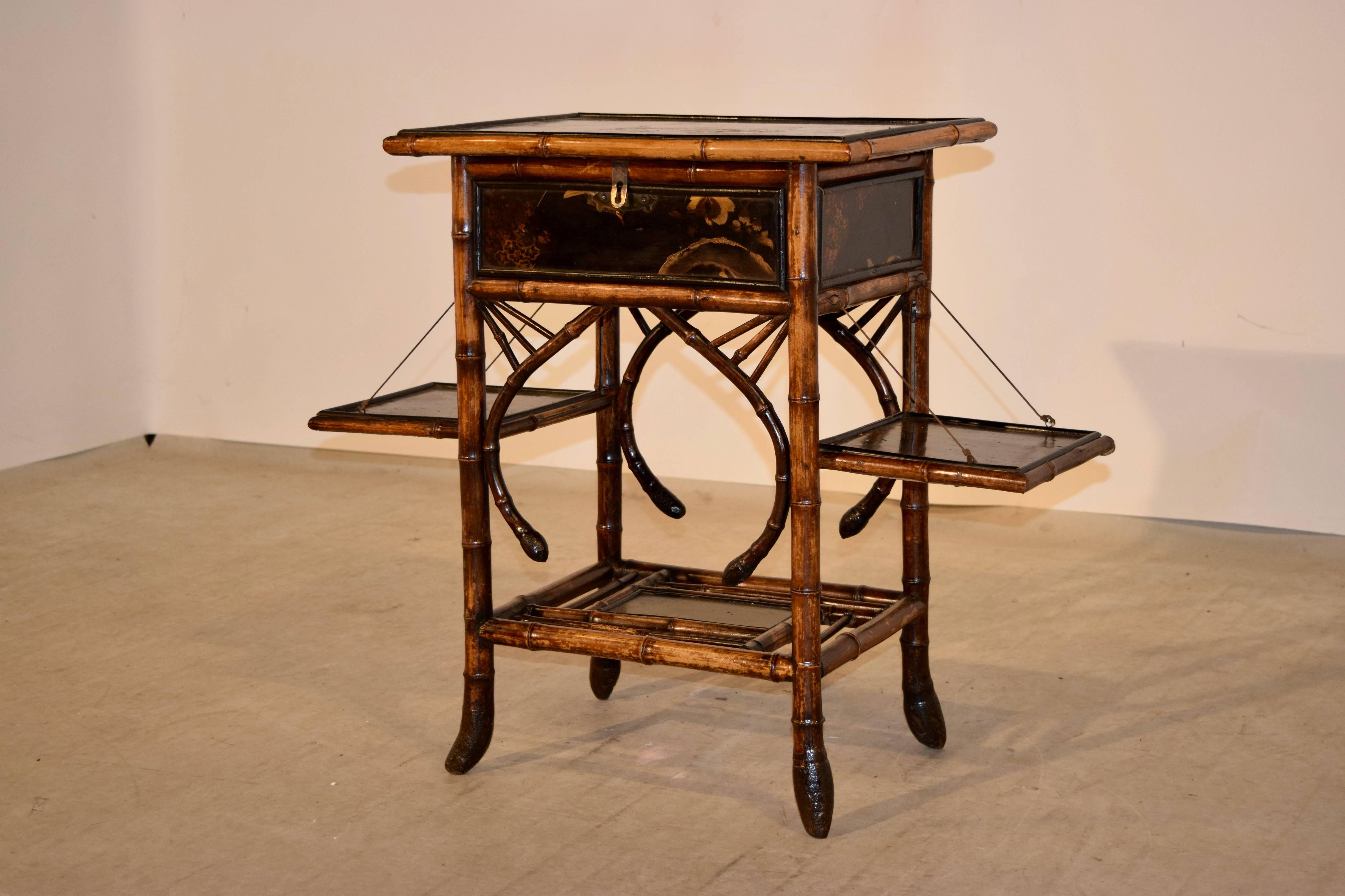 19th century bamboo sewing table from France with chinoiserie decoration on the top, sides, and shelves. The top lifts to reveal a silk upholstered compartment, which was used for ladies' sewing. Their is a lower shelf as well and two side shelves,