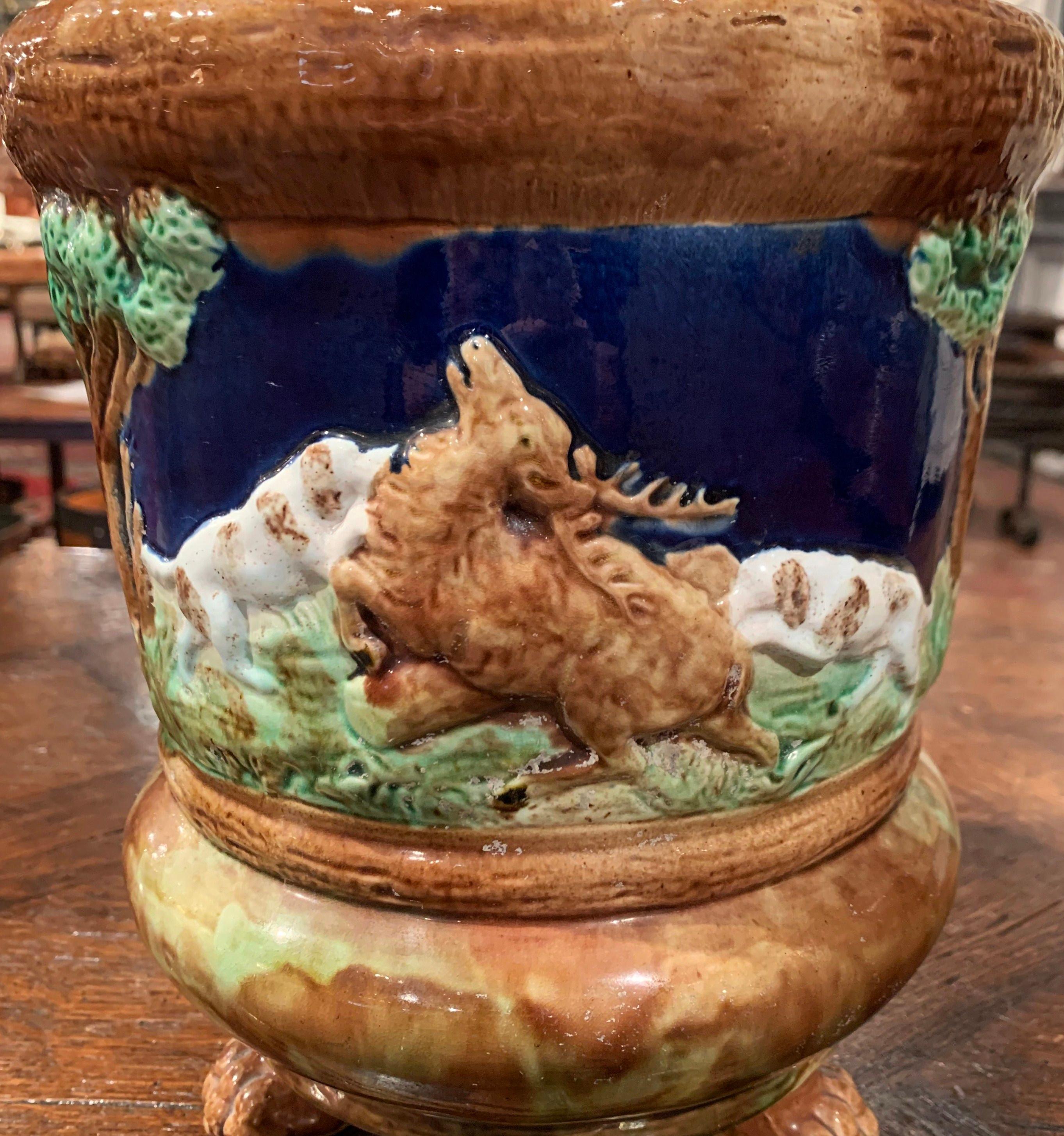 Crafted in Sarreguemines, France circa 1880, the colorful Majolica planter stands on three paw feet; it features a hunt scene in high relief with dogs chasing a deer and flanked by trees on both sides. The round faience cachepot is in excellent