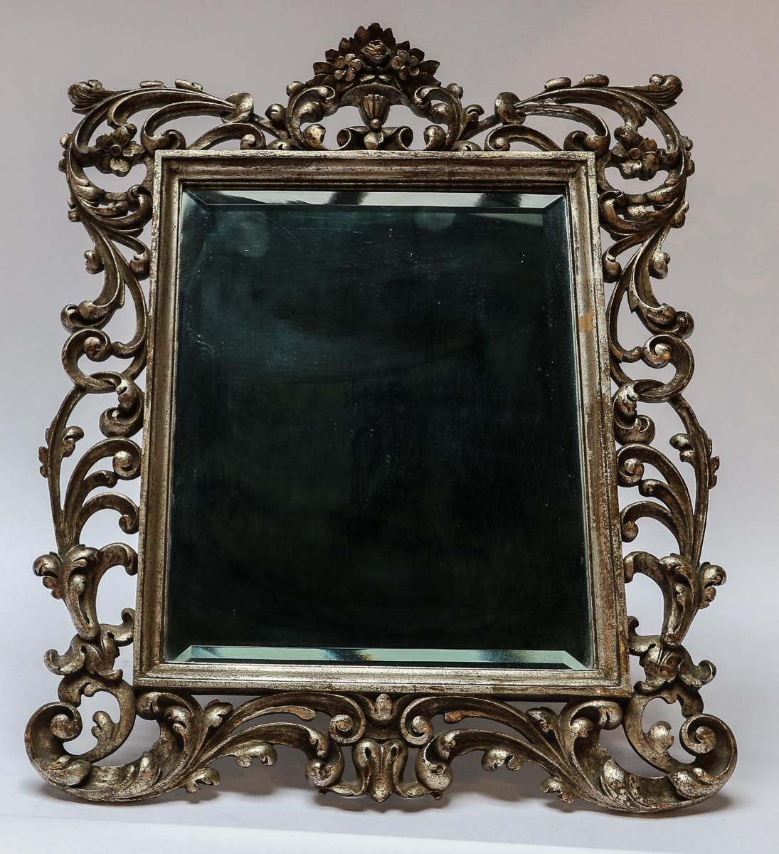 Ornately carved 19th century Baroque style vanity or wall mirror of silver giltwood and beveled glass. Can also be hung on the wall with the attached wire.