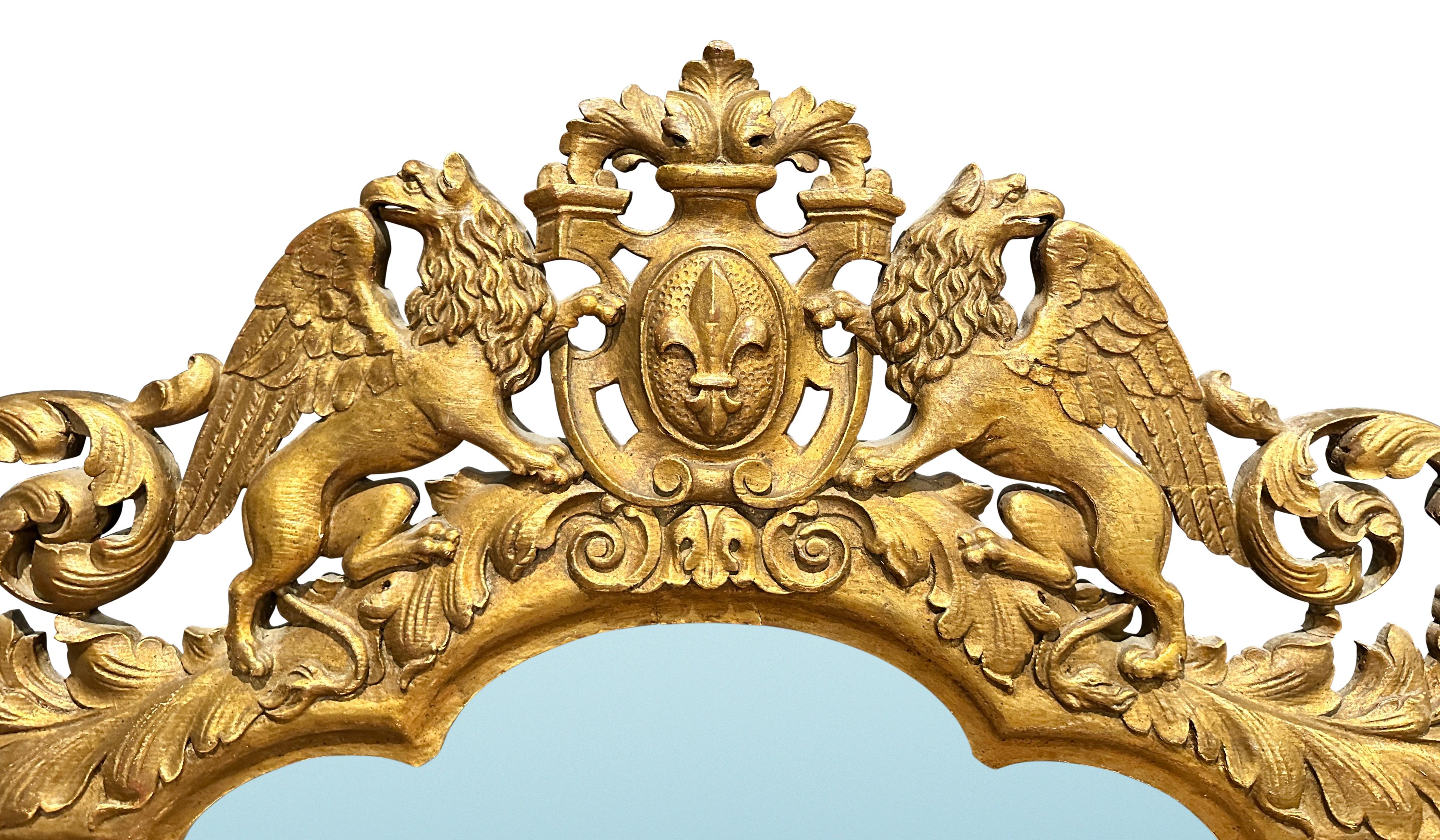 Miroir en bois sculpté et doré de belle qualité, avec deux griffons ailés flanquant un cartouche central contenant une fleur de lys. Le cadre sculpté et doré présente des rinceaux de rocaille et de feuillage autour de sculptures en forme de