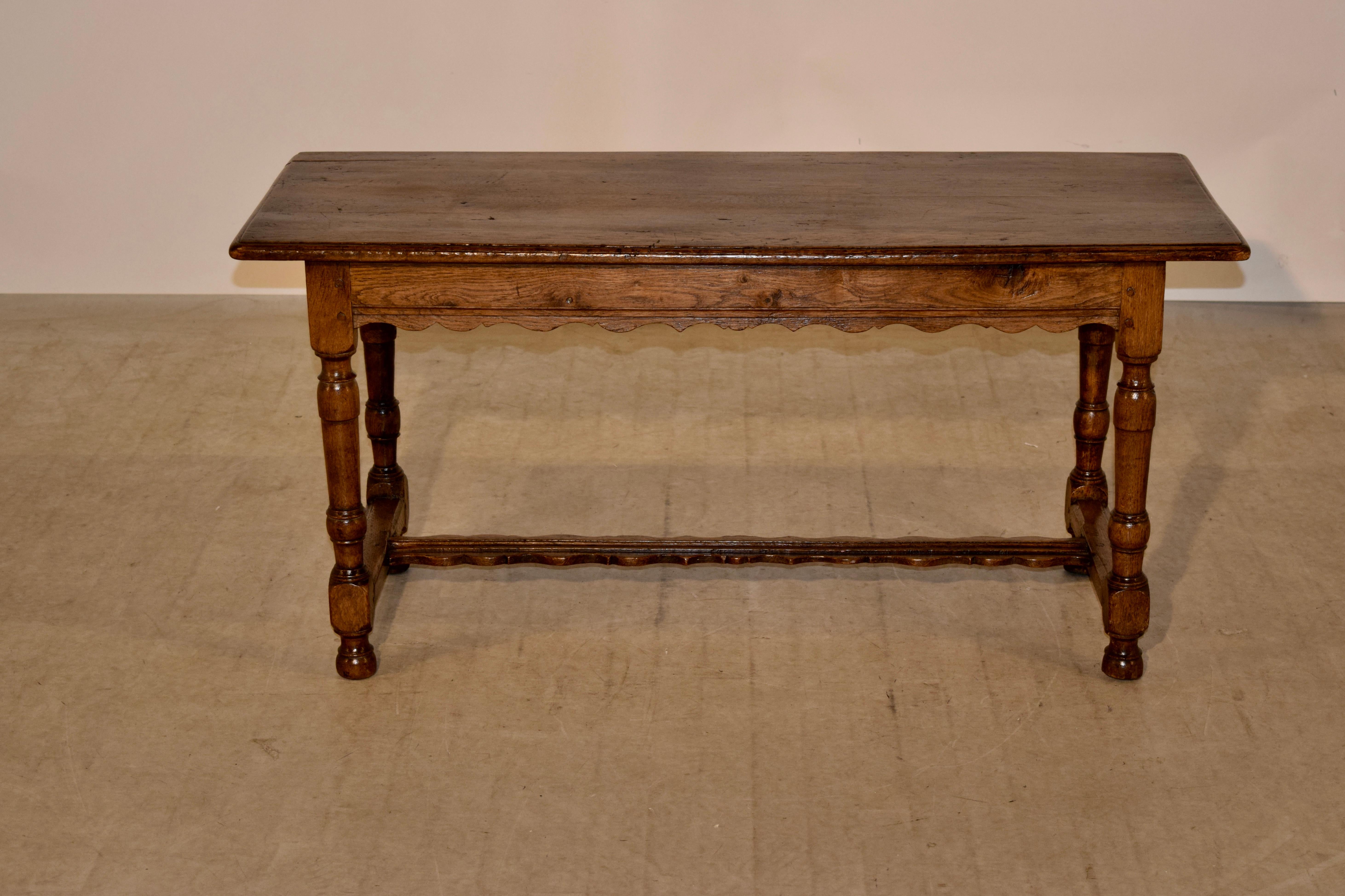 19th century bench from France made from oak. The top has a bevelled edge and follows down to a scalloped apron on three sides and a simple apron on the back, supported on hand turned legs joined by simple stretchers on the sides and a scalloped