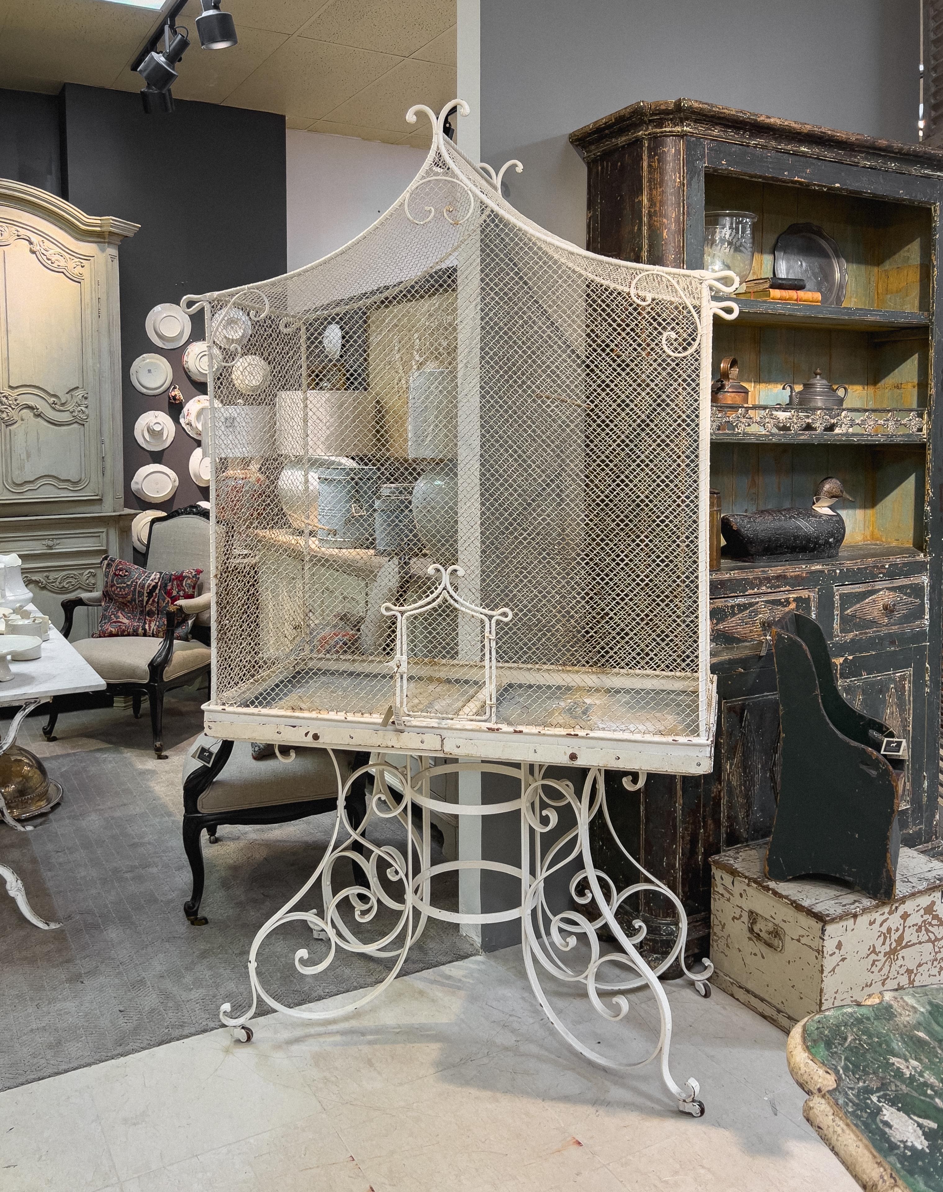 19th century French bird cage is nearly 7 feet tall, free standing bird house, stands on four intricate iron scroll legs connected with a double circular stretcher, and ending with rolling coasters. The wired bird habitat has a rectangular body and