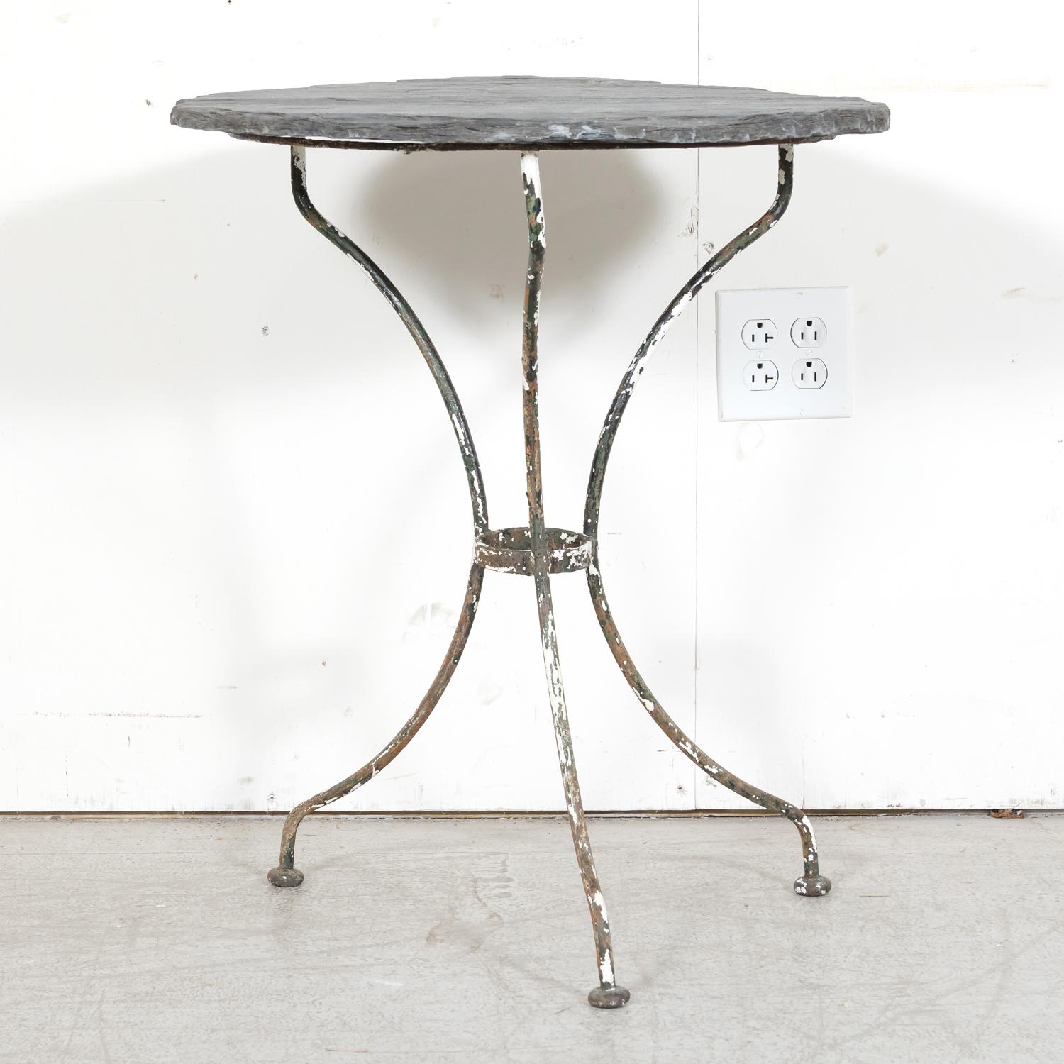 A 19th century French cast iron bistro or garden table, circa 1880s, featuring a slate top resting on a painted iron tri-form base. The base boasts three scrolled legs joined with a circular iron stretcher, adding both stability and visual appeal.