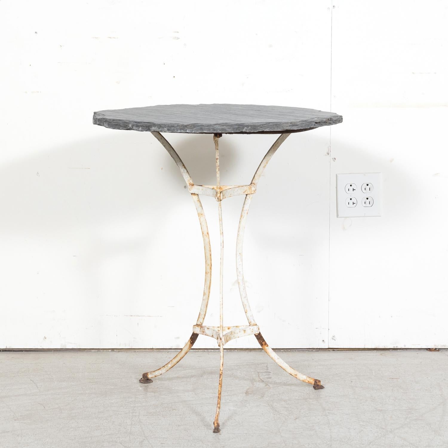 Tavolo da bistrot o da giardino in ghisa francese del XIX secolo, circa 1880, con piano in ardesia appoggiato su una base tripartita in ferro verniciato bianco. La base è formata da tre gambe a spirale unite da una barella circolare in ferro, che