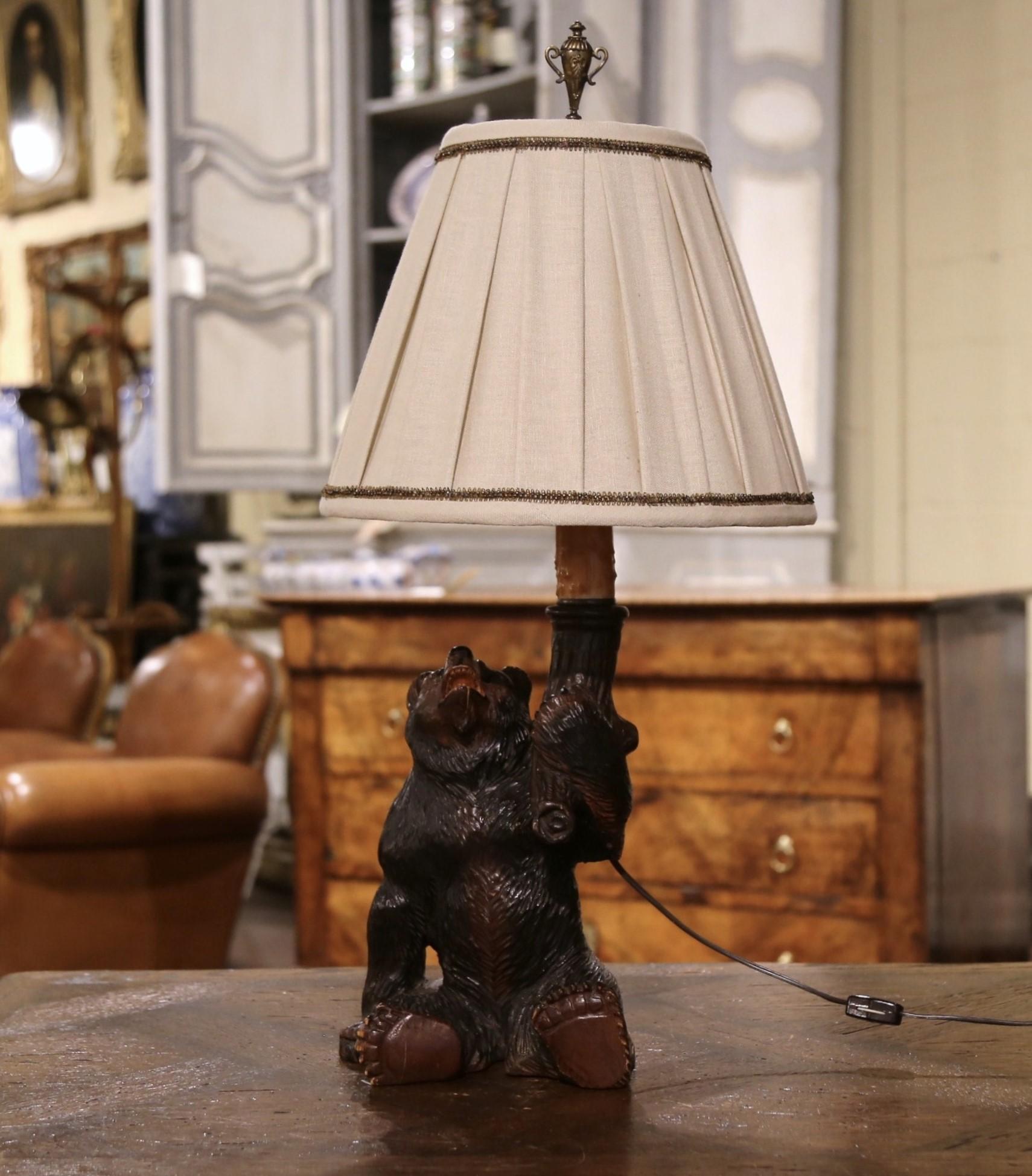 Decorate a ranch or hunting lodge with this elegant table lamp. Crafted in France circa 1880, this lamp depicts a carved sited bear holding a torch; the fixture has new wiring and is dressed with a real wax candle. The Black Forest fixture is in